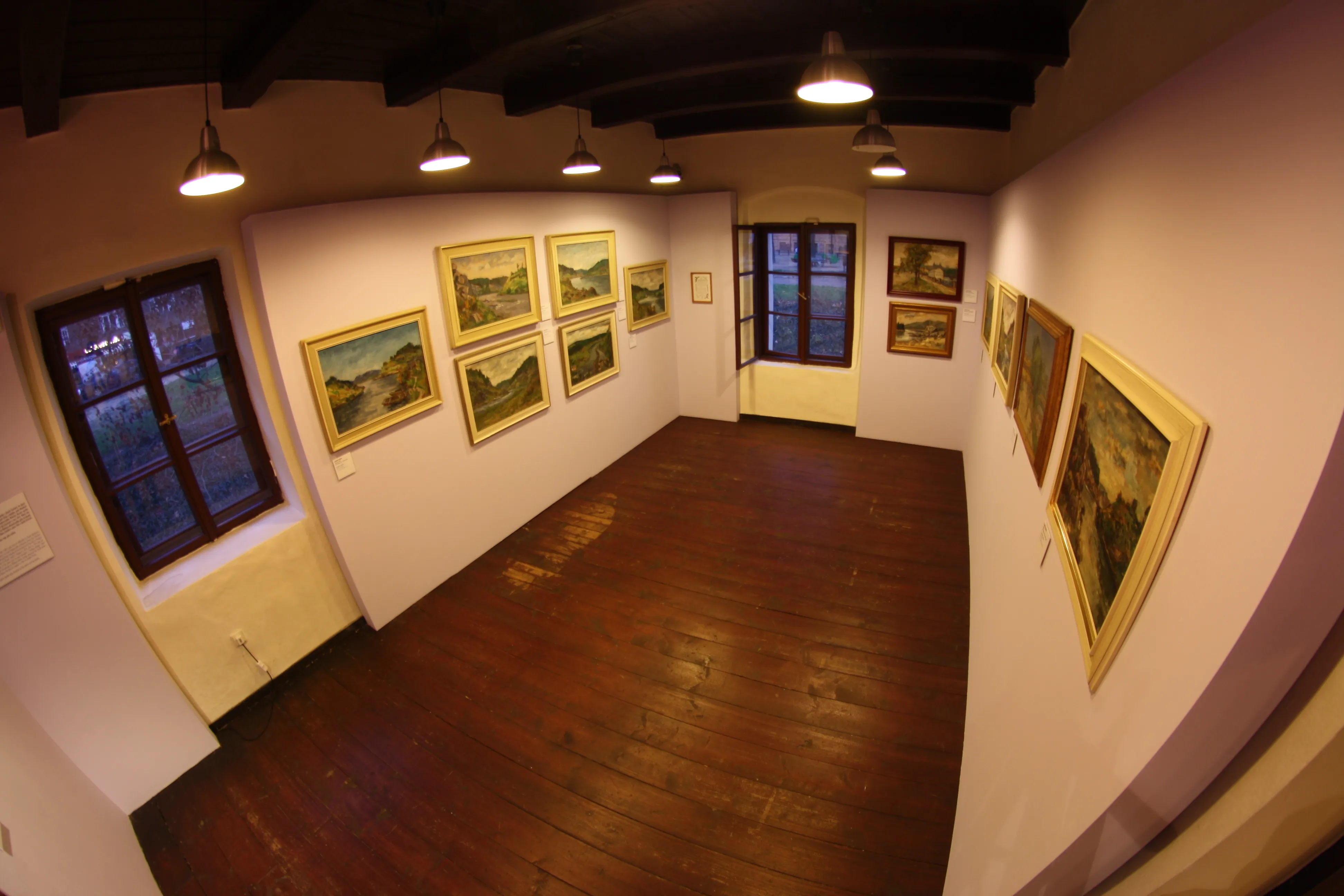 Galeria z drewnianą podłogą, białymi ścianami i oprawionymi obrazami pod lampami wiszącymi