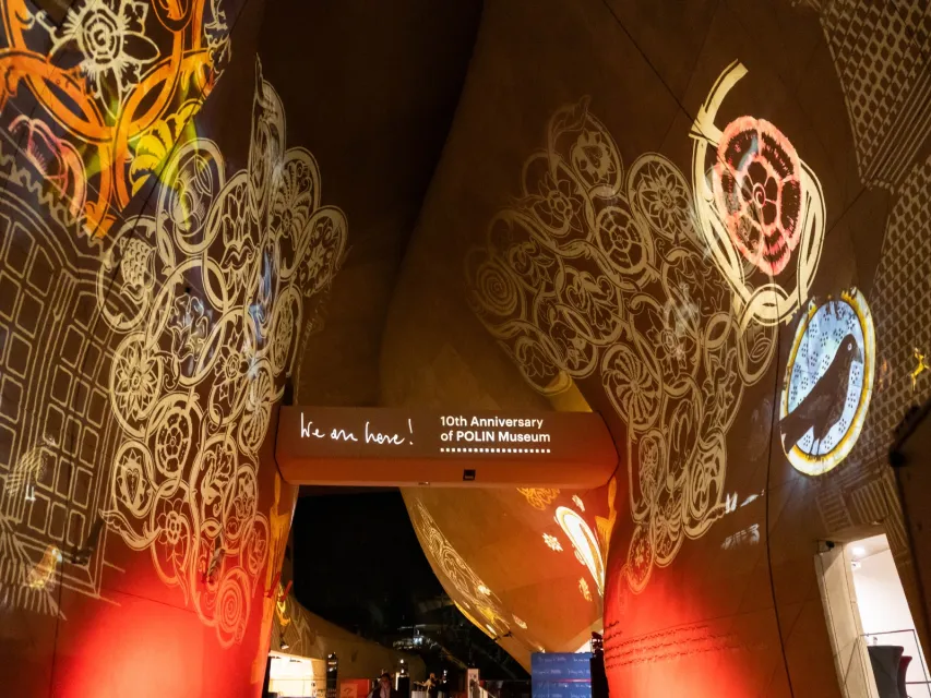 Geprojecteerde patronen op gebogen muren met een bord met de tekst '10e Verjaardag van het POLIN Museum'