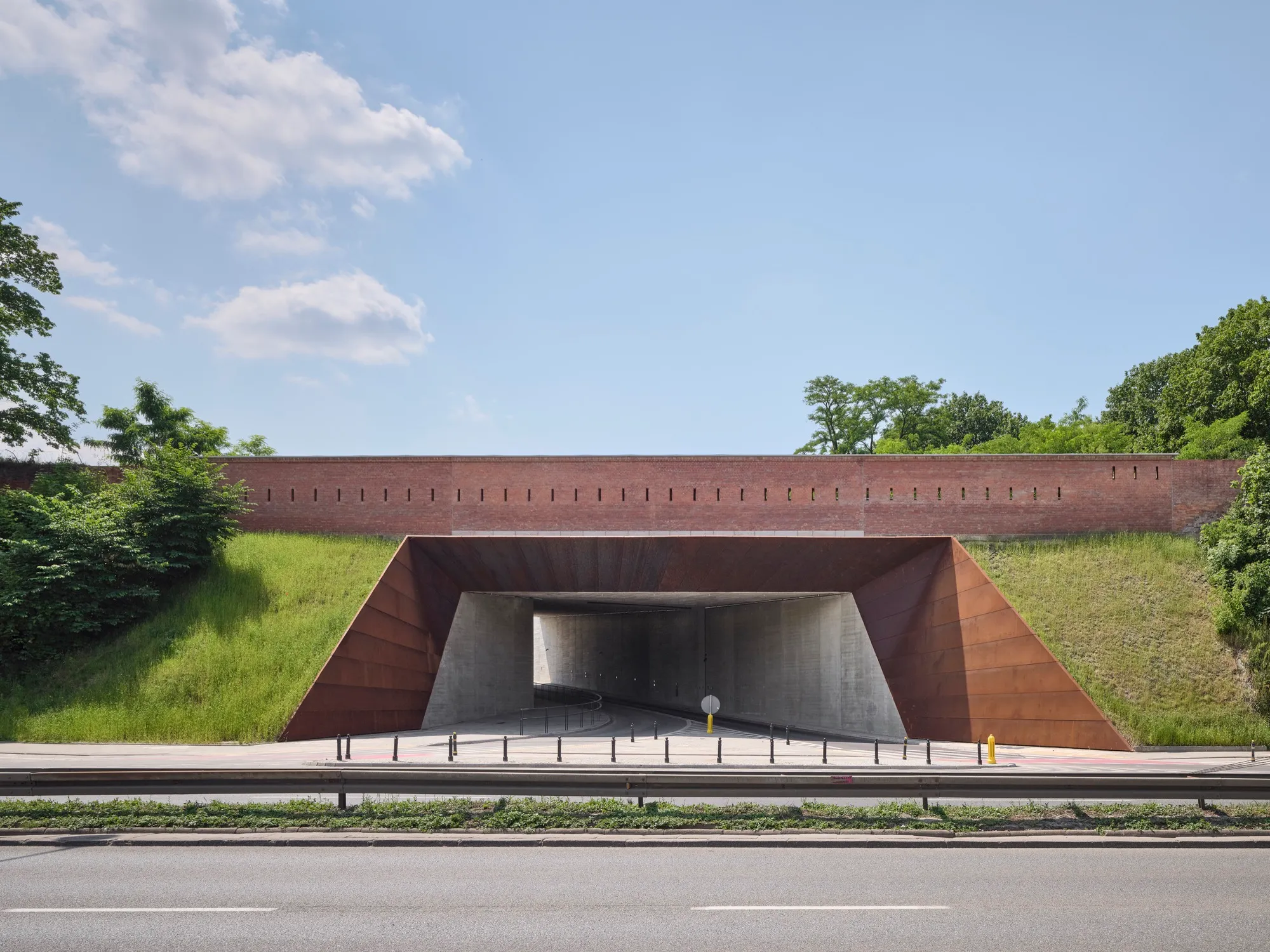 moderne museumingang met roestbruin stalen gevel en tunnel onder een grasheuvel