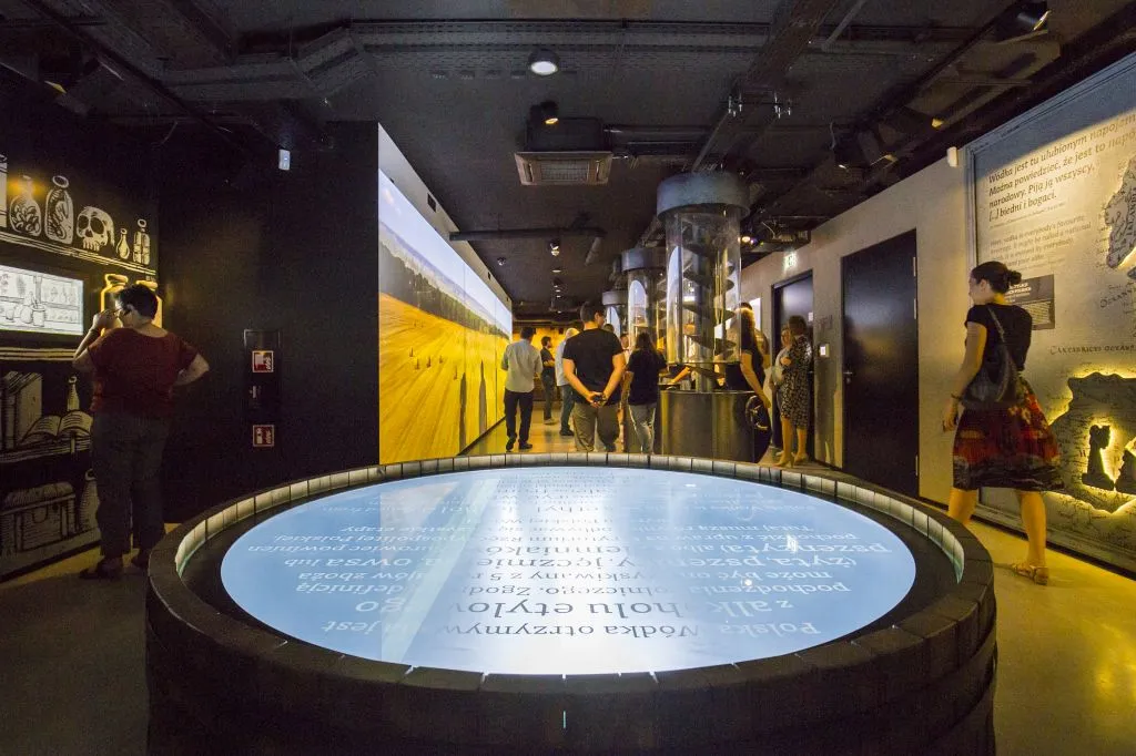 Interior del Museo Polaco del Vodka con una gran exhibición de barriles iluminados y visitantes caminando por la sala de exposiciones