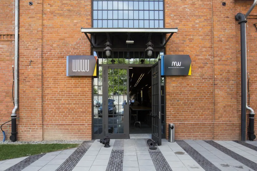 Entrada de edificio de ladrillos con puertas de cristal y dos letreros que muestran el logo 'Www'