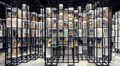 Filas de estanterías de metal negro llenas de botellas de vodka iluminadas en una galería de museo