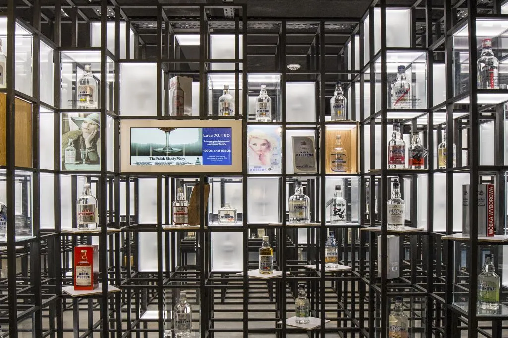 Botellas de vodka expuestas en una estructura de rejilla negra con estantes iluminados y paneles informativos