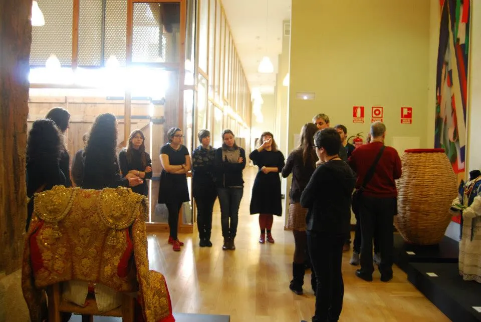 Visitors in a museum gallery viewing traditional artifacts including an ornate chair and a large woven basket