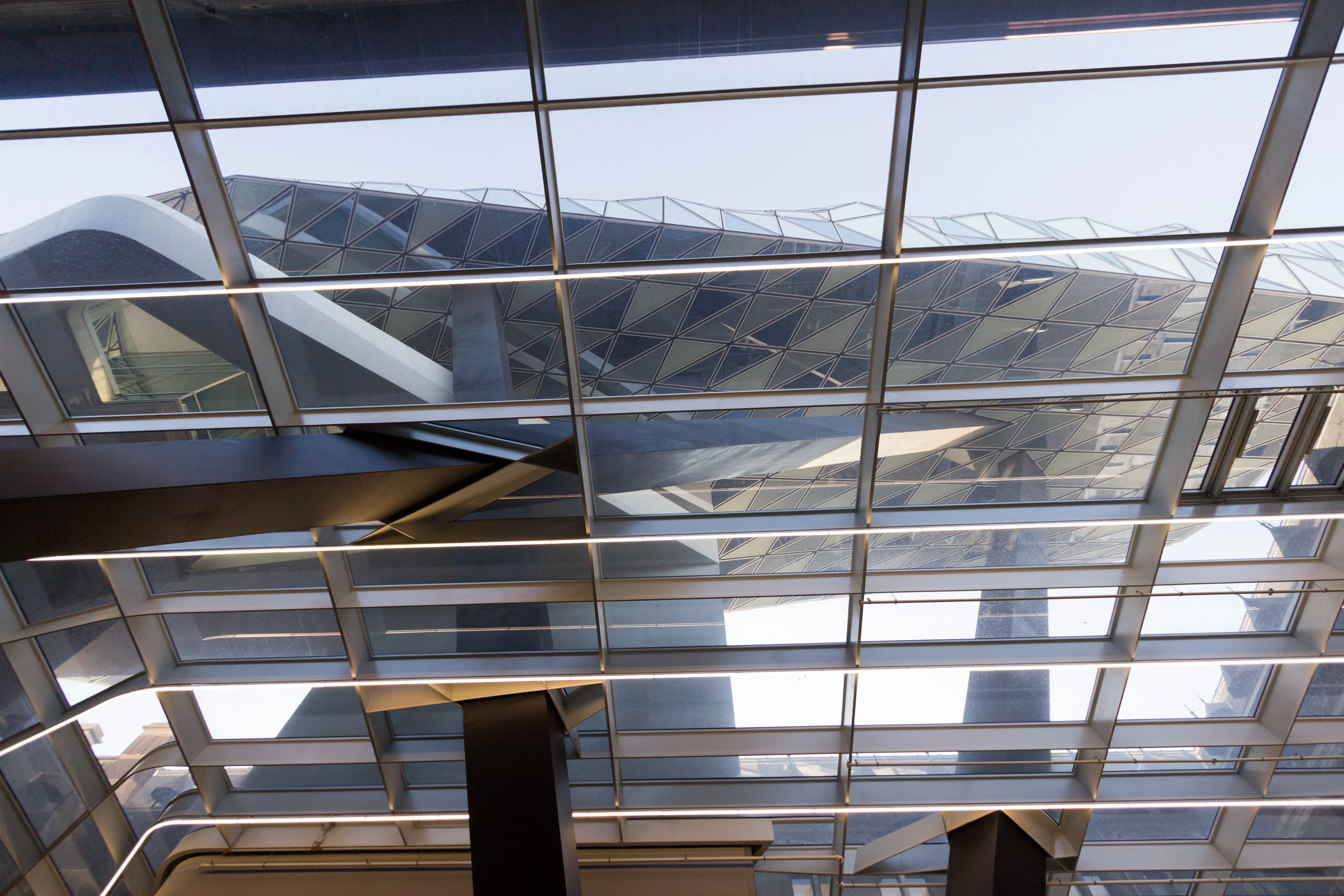 Vista hacia arriba a través de un techo de rejilla de cristal hacia la extensión de cristal facetado con forma de diamante del Havenhuis de Amberes