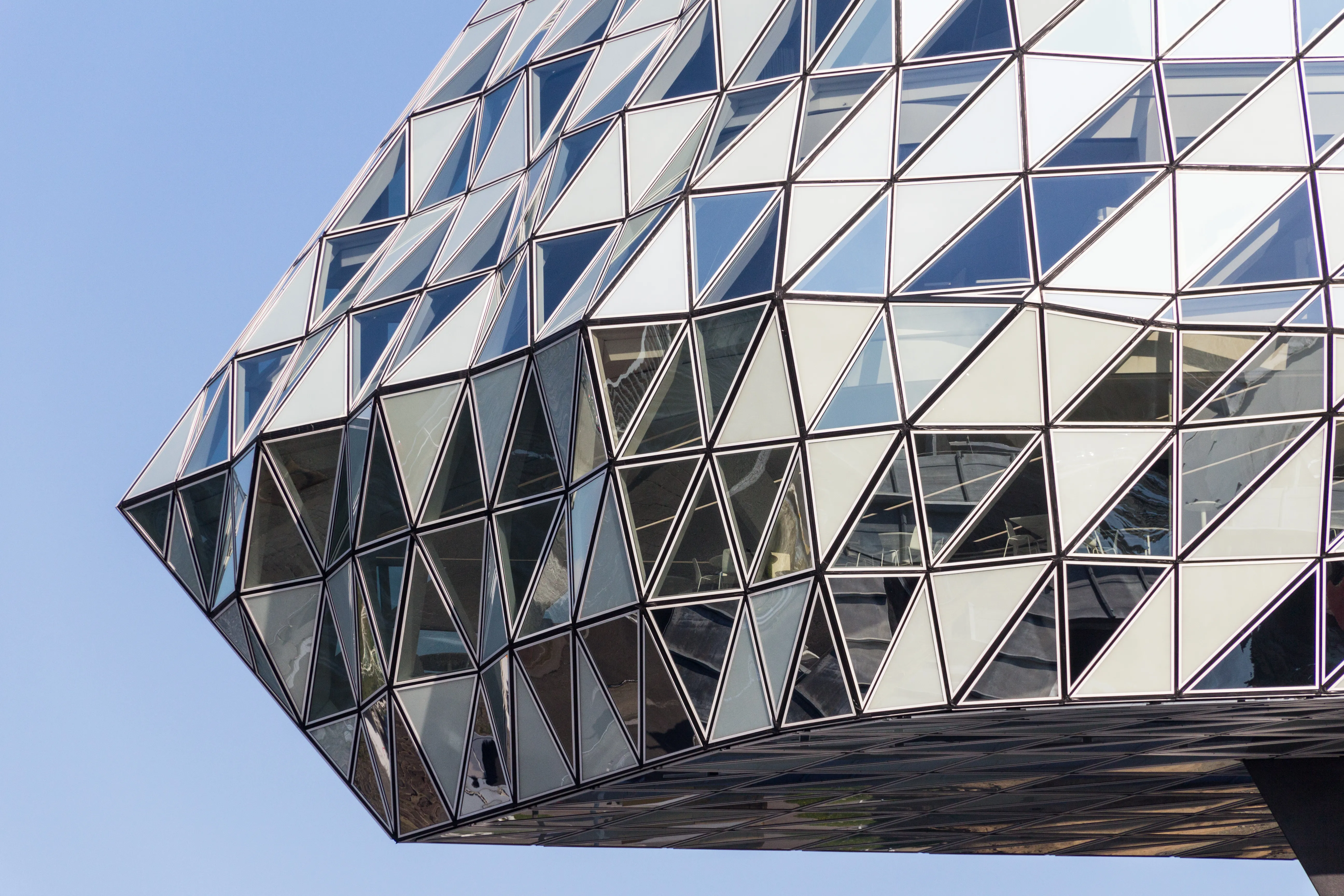 Primer plano de la fachada de cristal triangular cristalina del Port House de Amberes contra un cielo azul