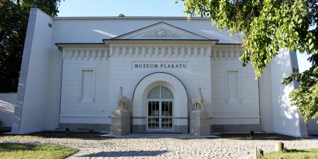 White classical building with 'MUZEUM PLAKATU' inscription above arched entrance and two stone sculptures