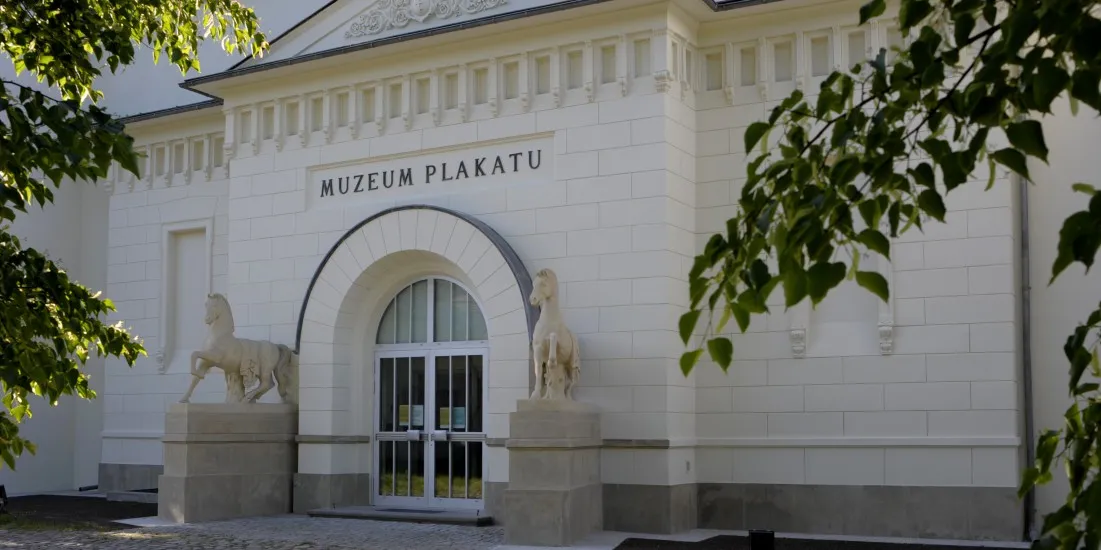 White building facade with arched entrance, two stone horse sculptures, and the text 'MUZEUM PŁAKATU' above the door