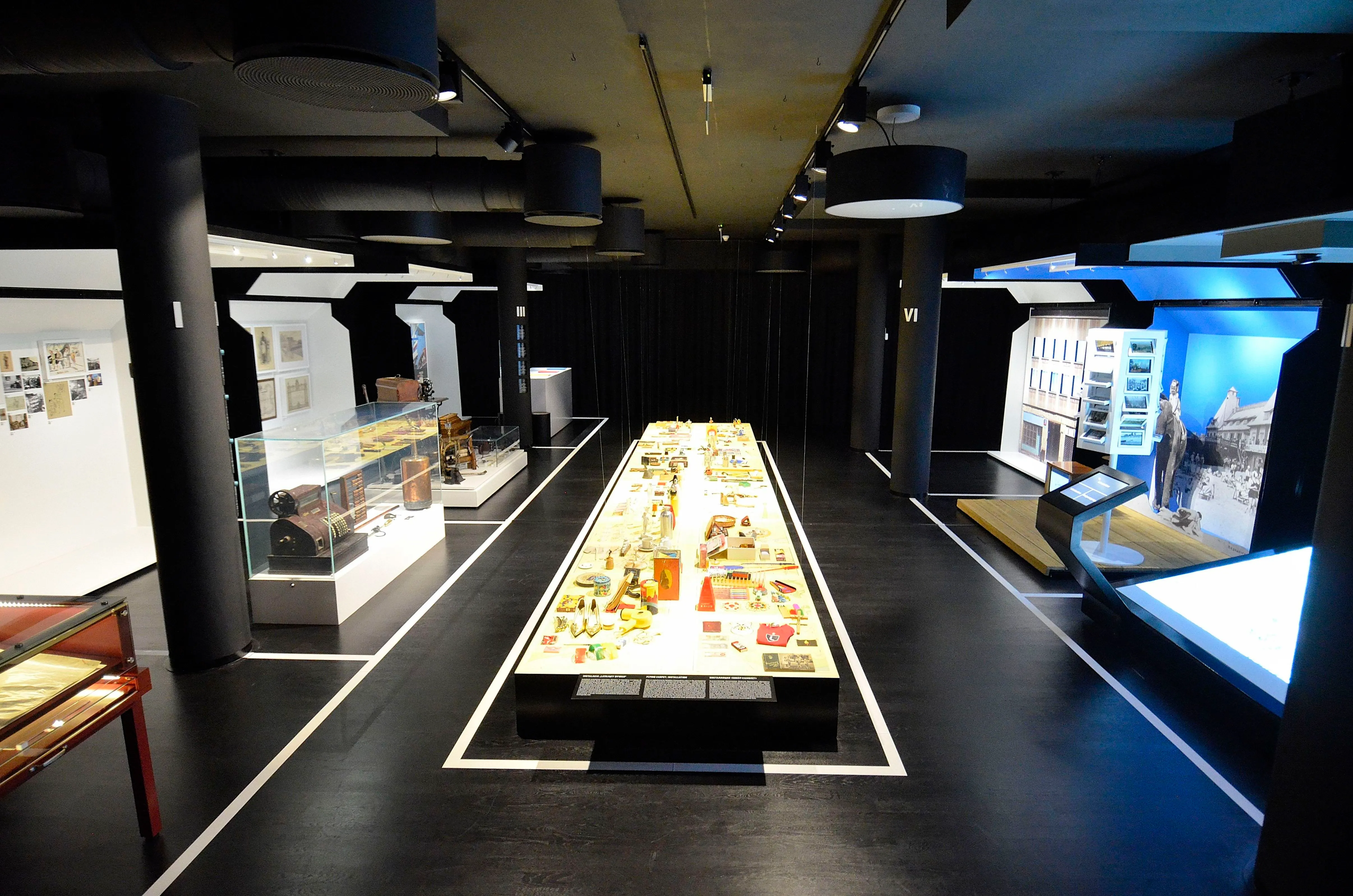 Wnętrze muzeum z długą centralną gablotą, szklanymi gablotami i nowoczesnym oświetleniem