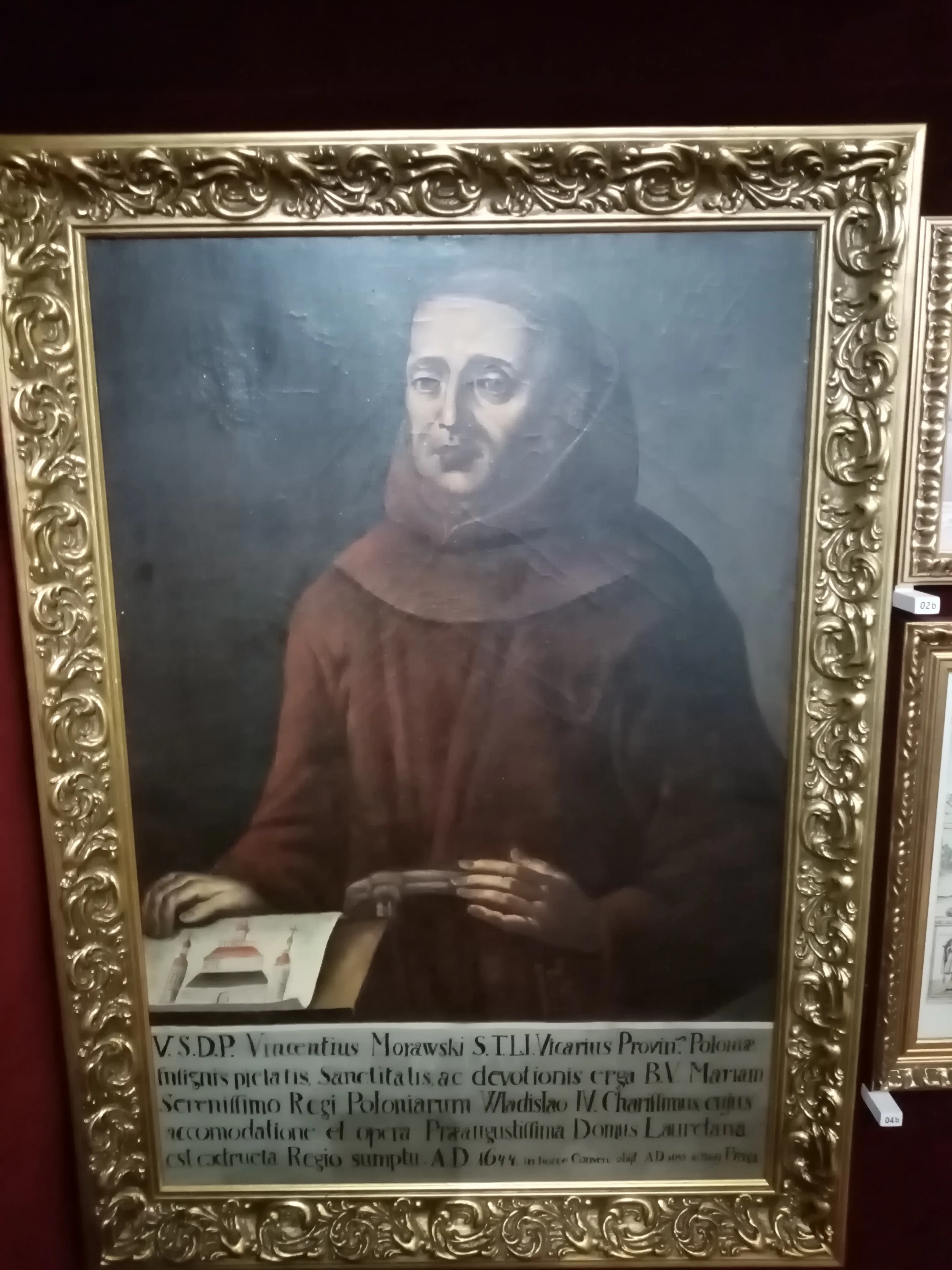 portret w ramie mężczyzny w brązowej szacie ze złotą, ozdobną ramą i łacińskim napisem poniżej