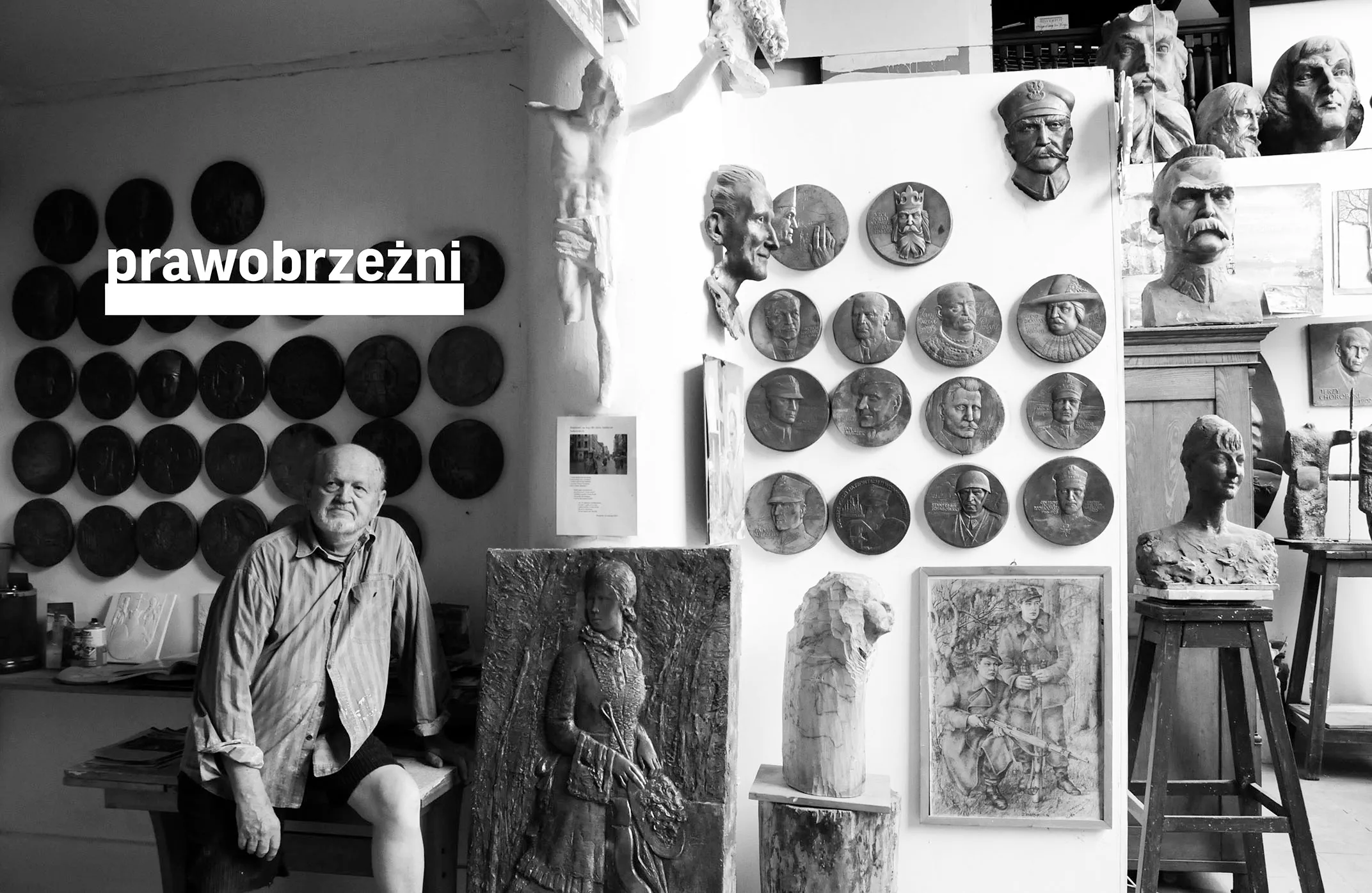 black and white photo of artist in studio with sculptures and wall-mounted reliefs