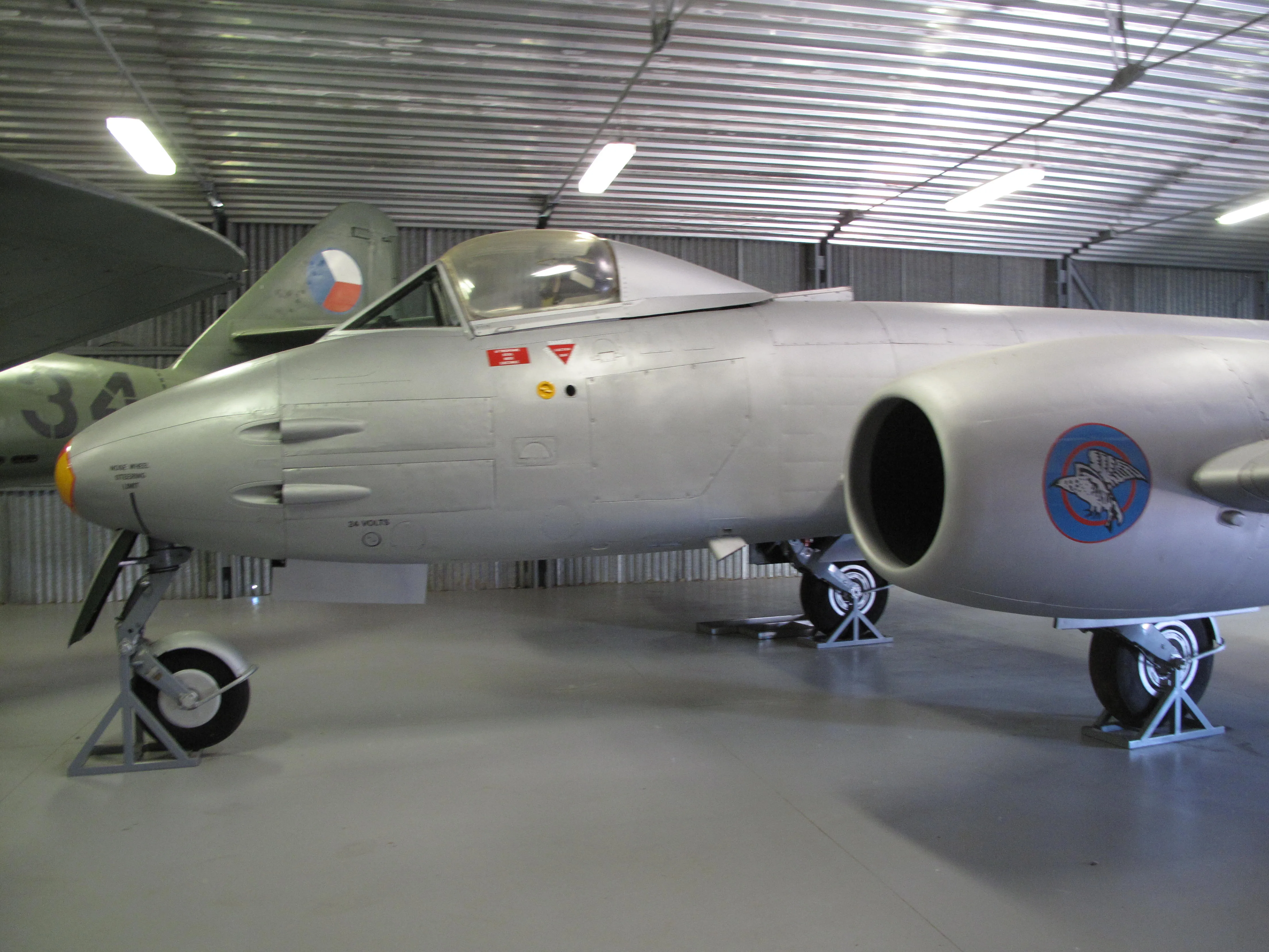 Zilveren straalvliegtuig met rondel-embleem tentoongesteld in een museumhangar