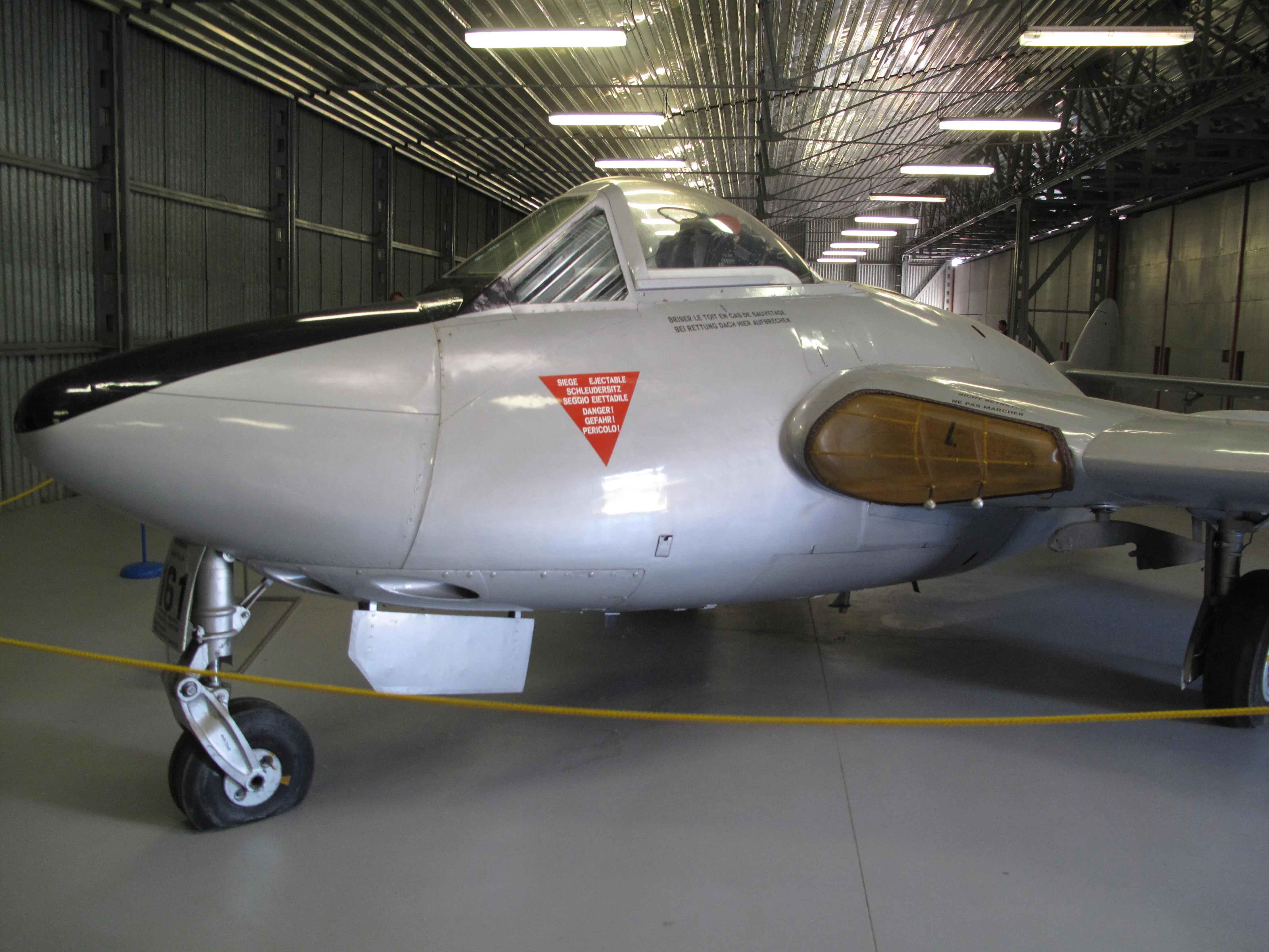 Zilveren straalvliegtuig met rode waarschuwingstriangel op de neus, tentoongesteld in een museumhangar.