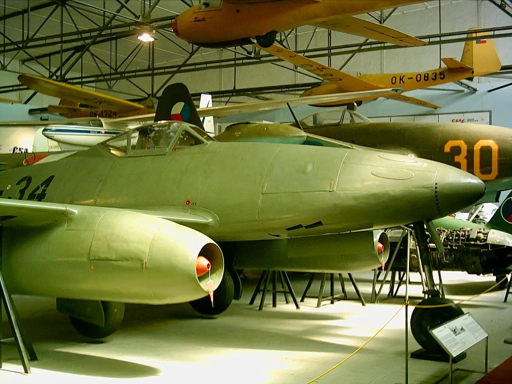 Een groene militaire straaljager tentoongesteld in een museumhangaar met andere vliegtuigen op de achtergrond