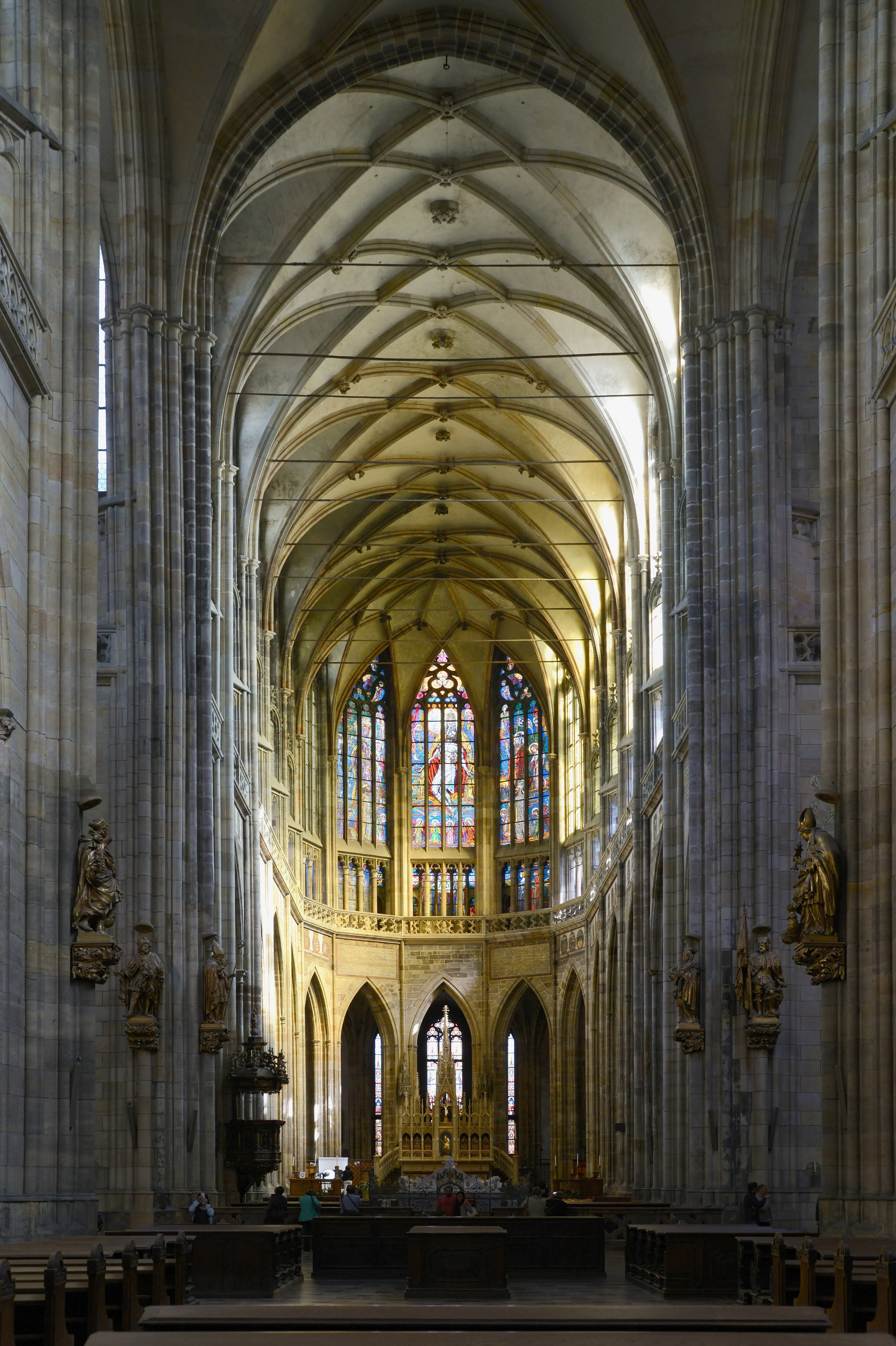 Interior of St. Vitus Cathedral with high stone arches, stained glass windows, and wooden pews