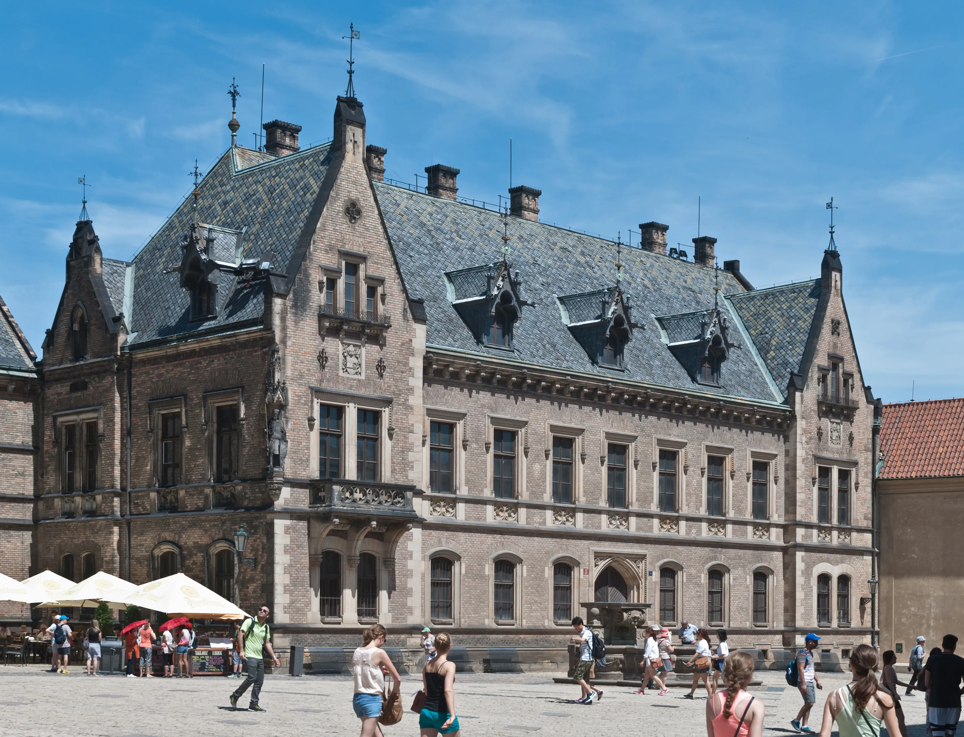 Een groot historisch gebouw met een grijs leien dak en sierlijk steenwerk op de binnenplaats van Praagse Burcht