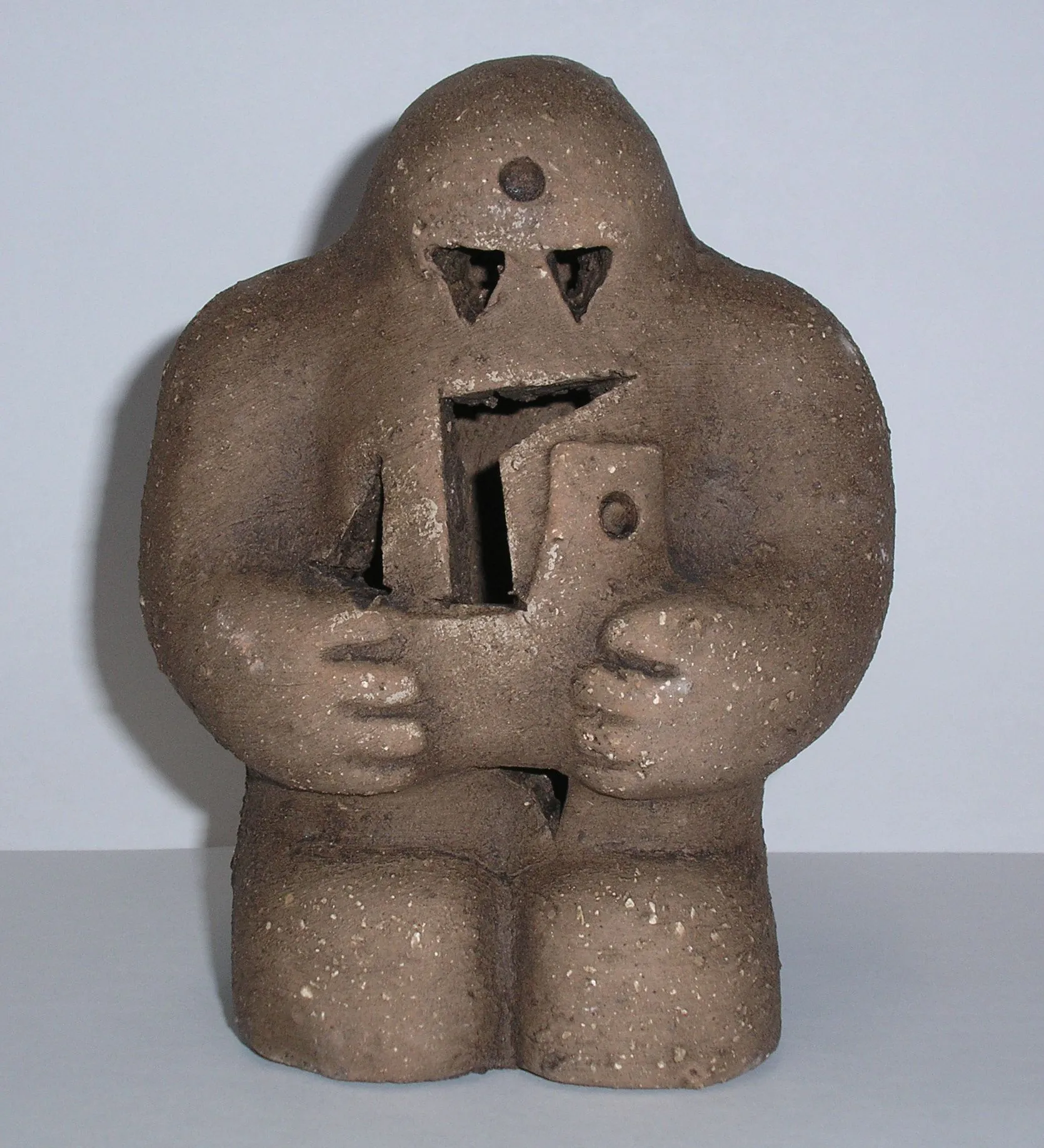 A brown ceramic sculpture of a stylized figure holding a geometric object