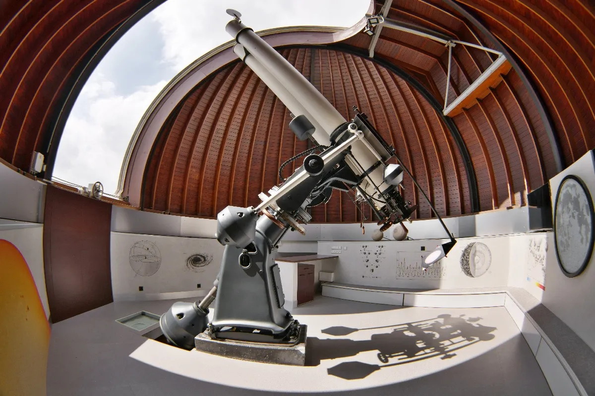 A large telescope inside a planetarium with a curved wooden dome and circular displays on the walls