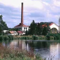 Het Praagse Waterleidingmuseum met een hoge bakstenen schoorsteen en gebouwen die in het water worden weerspiegeld