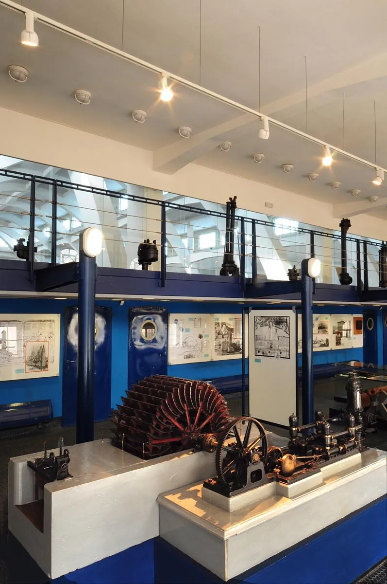 Historische waterpompen en machines tentoongesteld in een museumzaal met blauwe muren en informatieve panelen