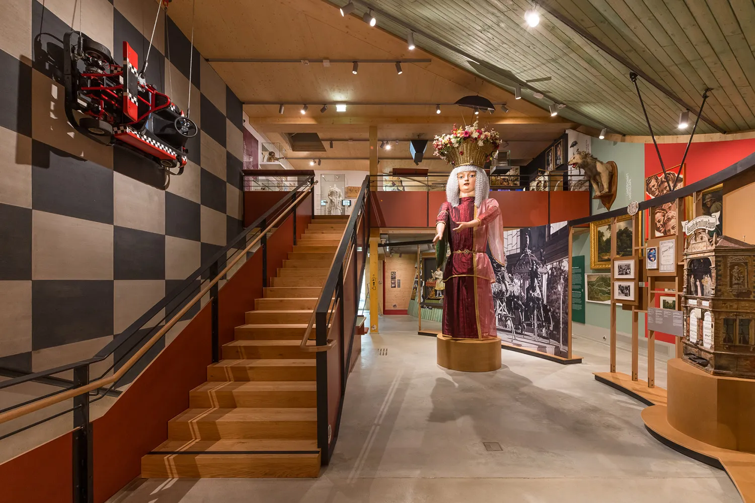 Wnętrze Pratermuseum ze schodami, w kratkę ścianą i manekinem w czerwonej sukience