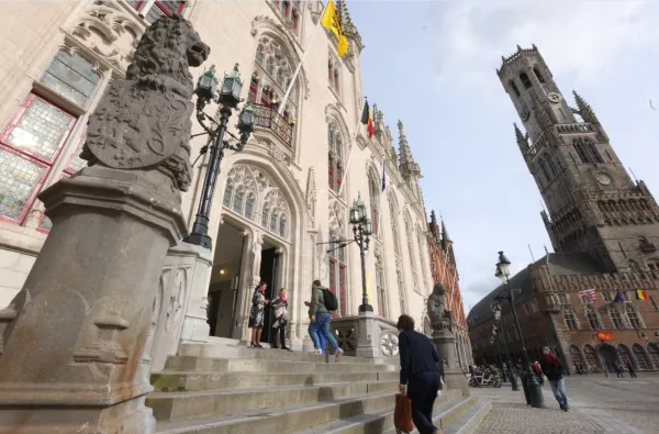 Fachada neogótica del Palacio Provincial de Brujas con una estatua de león de piedra sobre un pedestal en primer plano, gente en las escaleras y la torre del campanario visible al fondo.