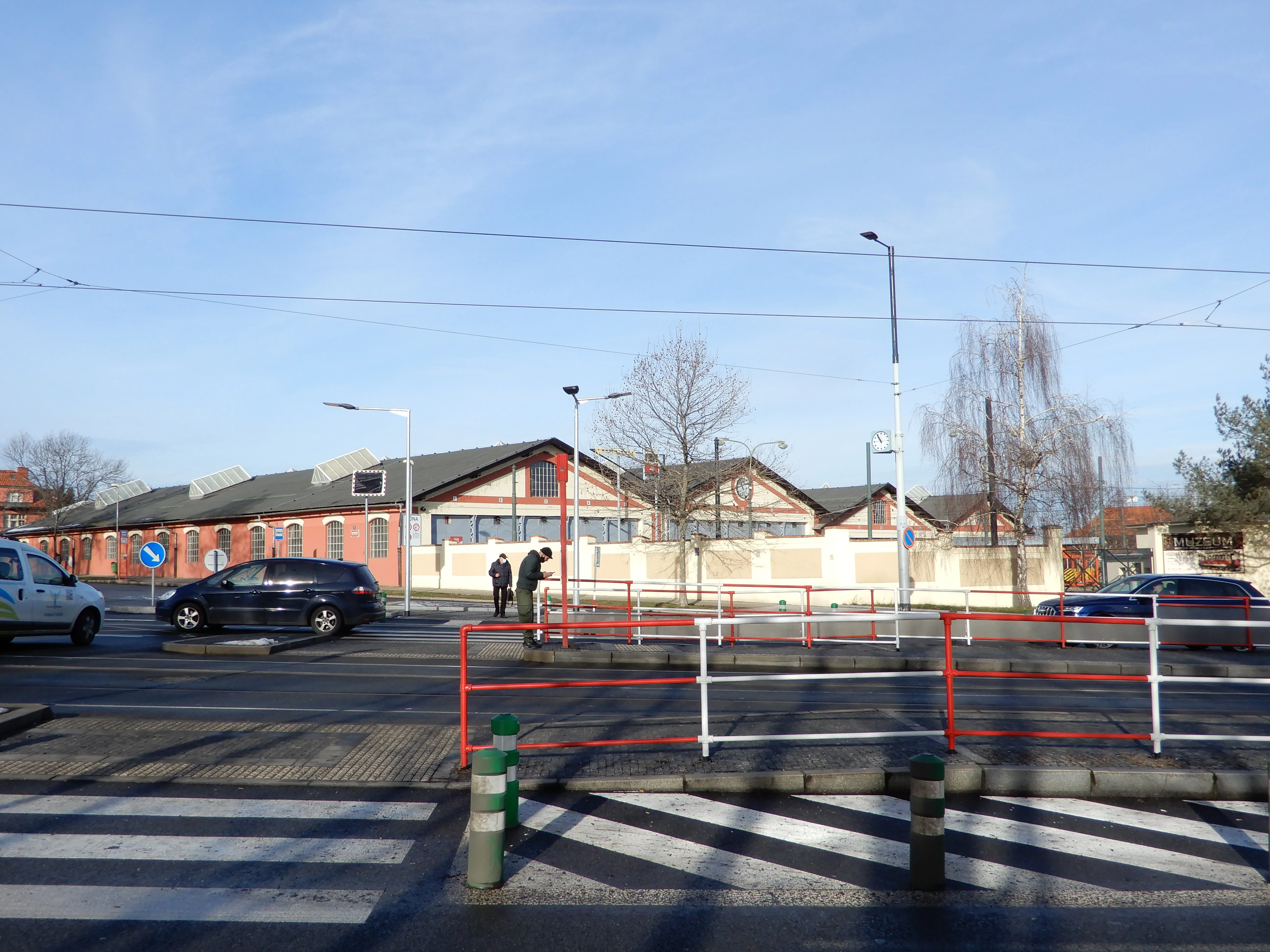 exterior of a brick building with a sloped roof, surrounded by a road with cars and a pedestrian crossing