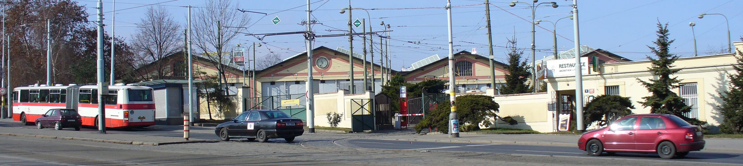 Historic tram depot buildings with a red and white tram parked in front, surrounded by trees and utility poles.