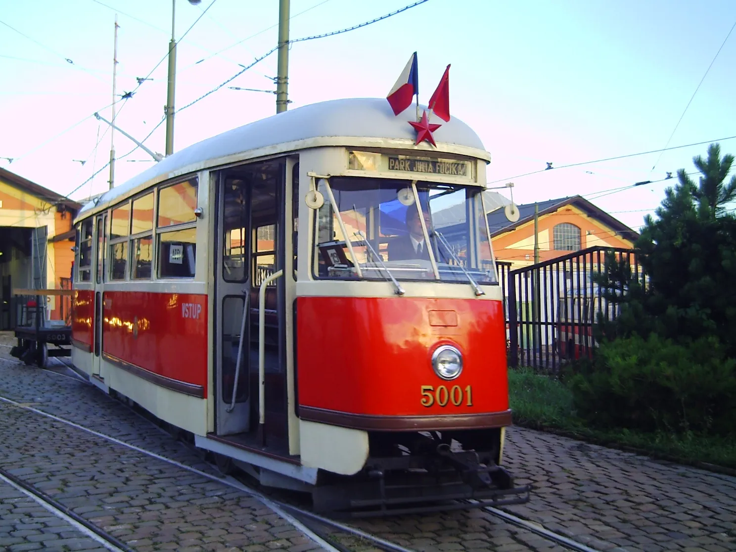 A red and cream vintage tram numbered 5001 on tracks with a Czech flag and red star on its roof