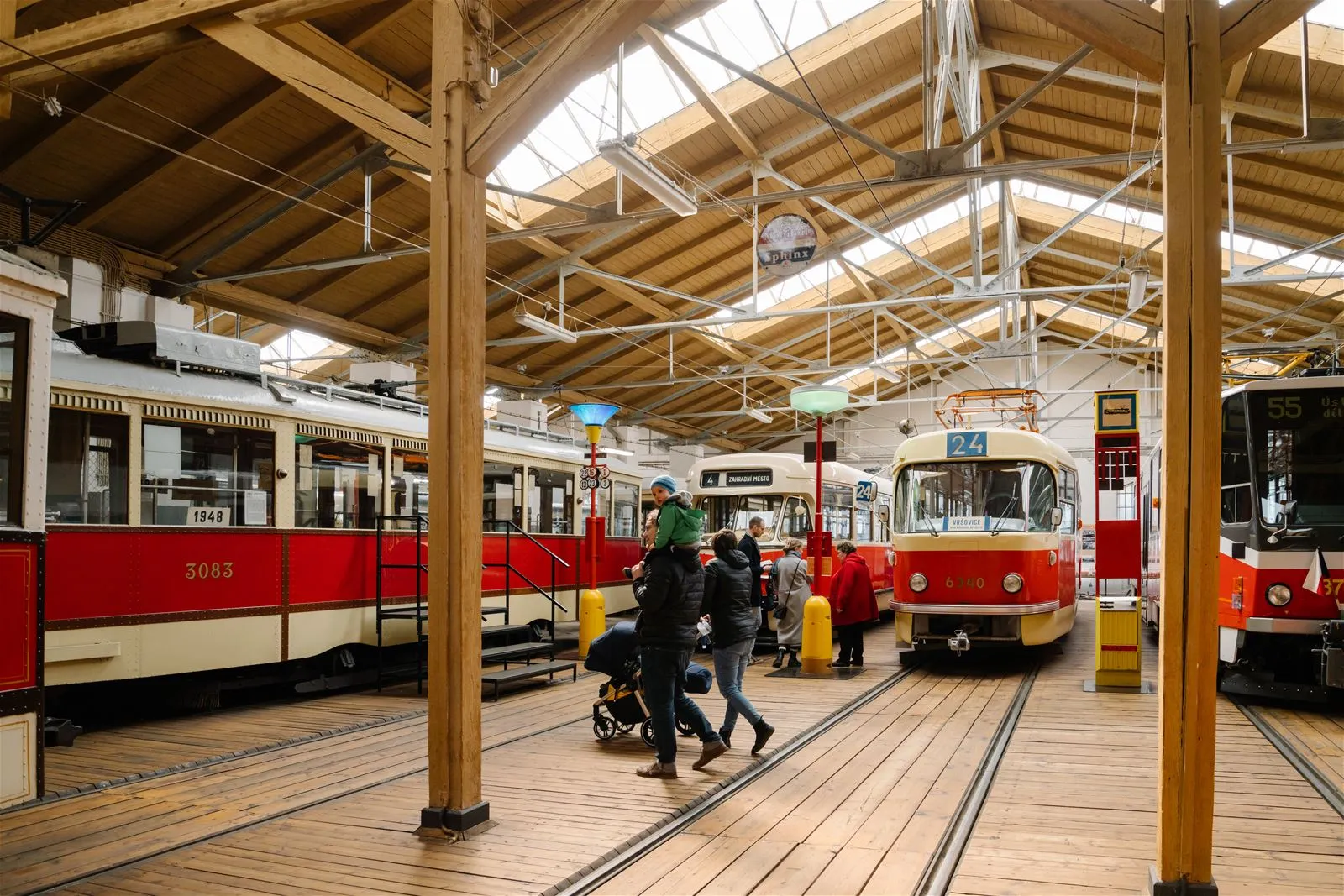 Interior of a museum with historic trams on tracks, wooden beams, and visitors walking