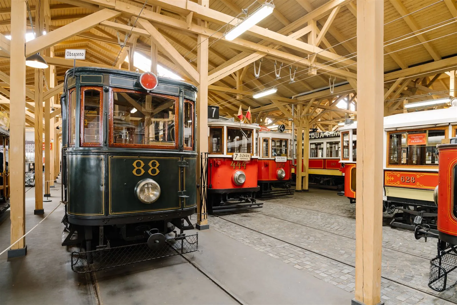 Green vintage tram numbered 88 displayed inside a large wooden-trussed hall with other historic trams