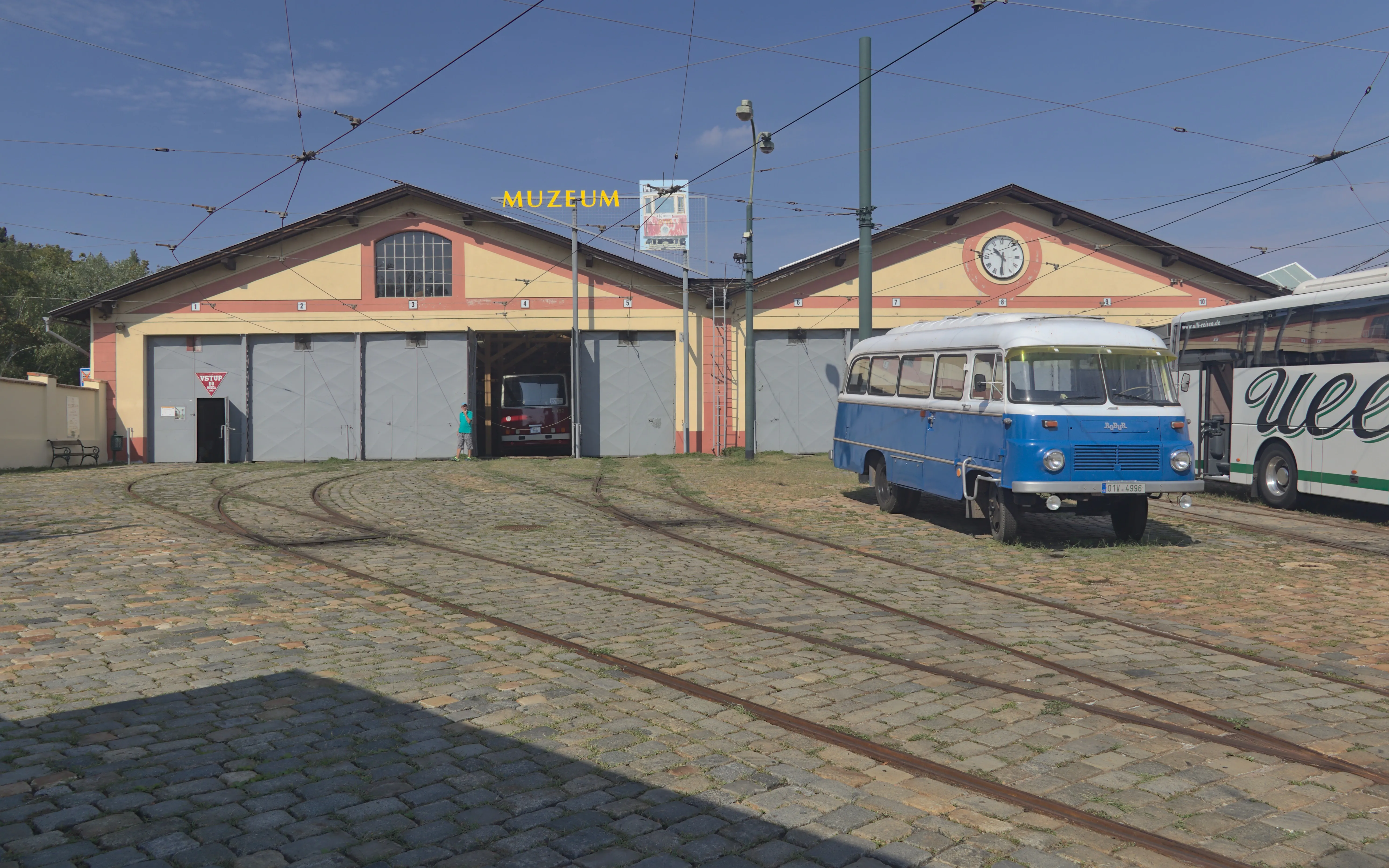 blue and white vintage bus parked in front of a large building with tram tracks on the ground