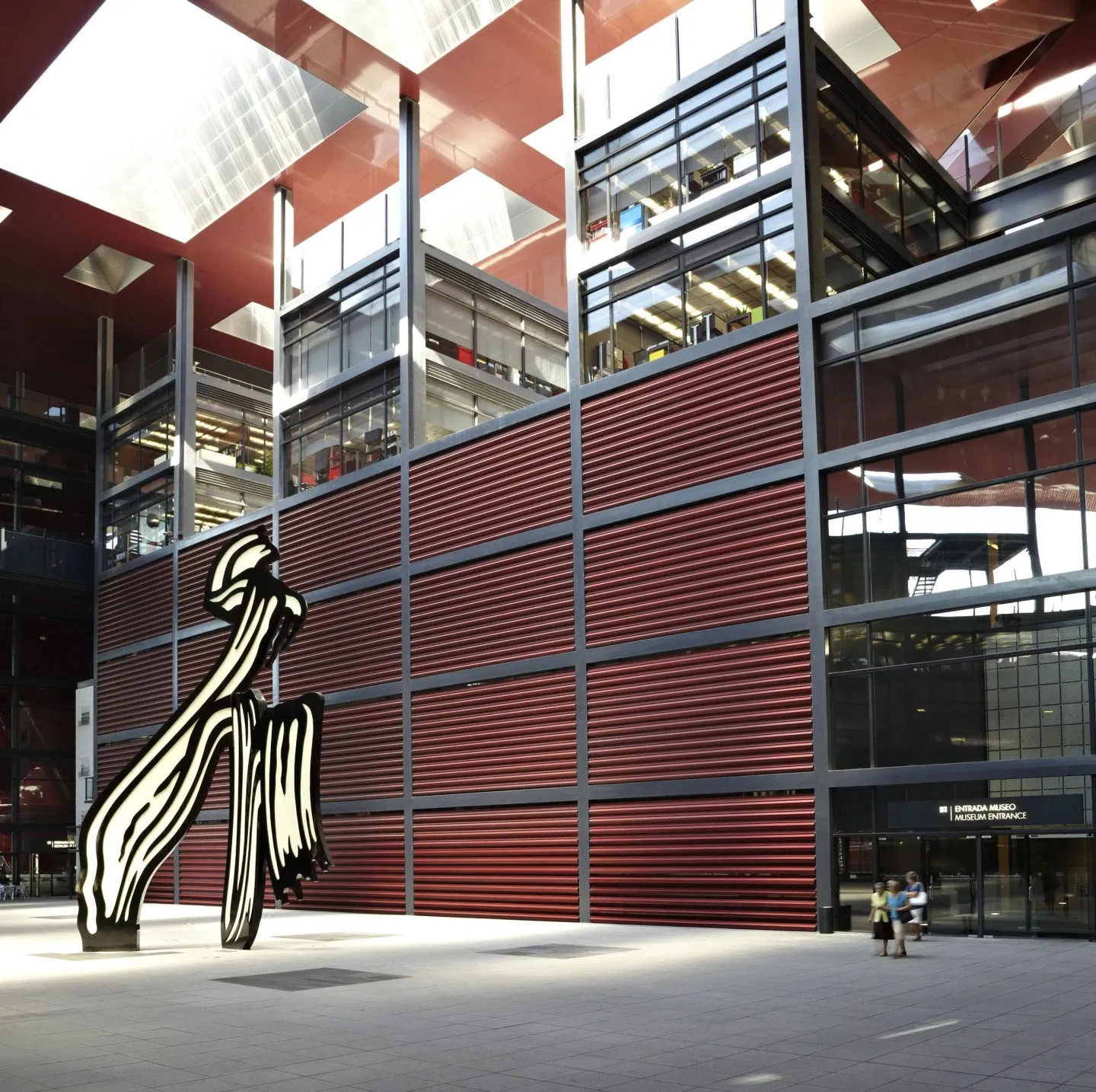 Edificio moderno con fachada de lamas rojas y gran escultura abstracta delante