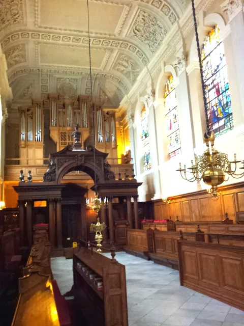Interior de una capilla con bancos de madera, un gran órgano de tubos en la galería, vidrieras y un ornamentado techo de yeso blanco