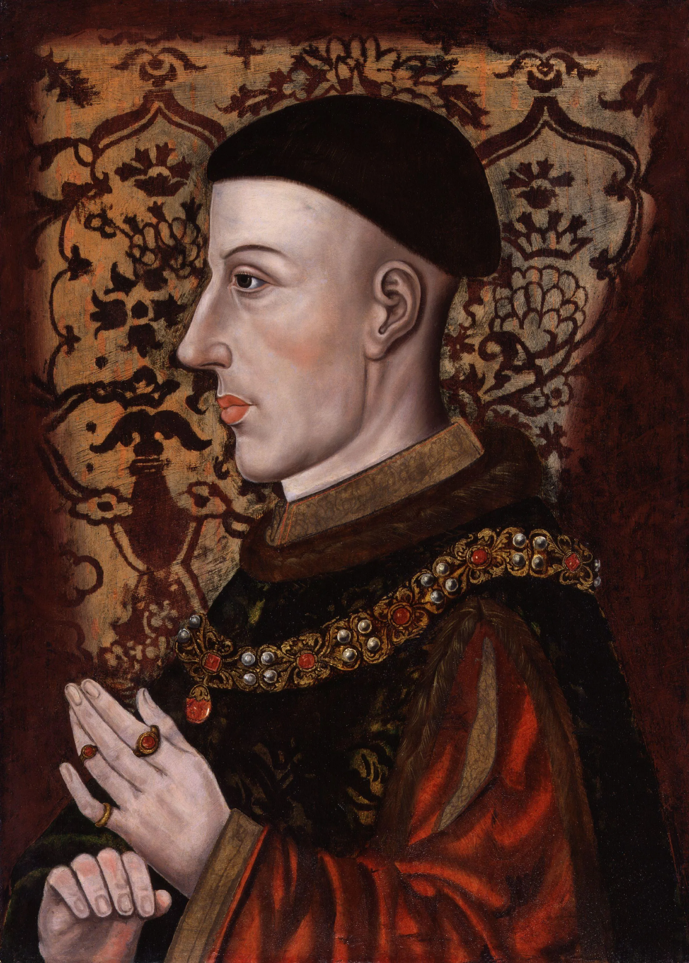 Retrato del rey Enrique V de perfil, vistiendo una gorra negra y túnicas rojas con un collar de joyas, con las manos juntas en oración sobre un fondo estampado.