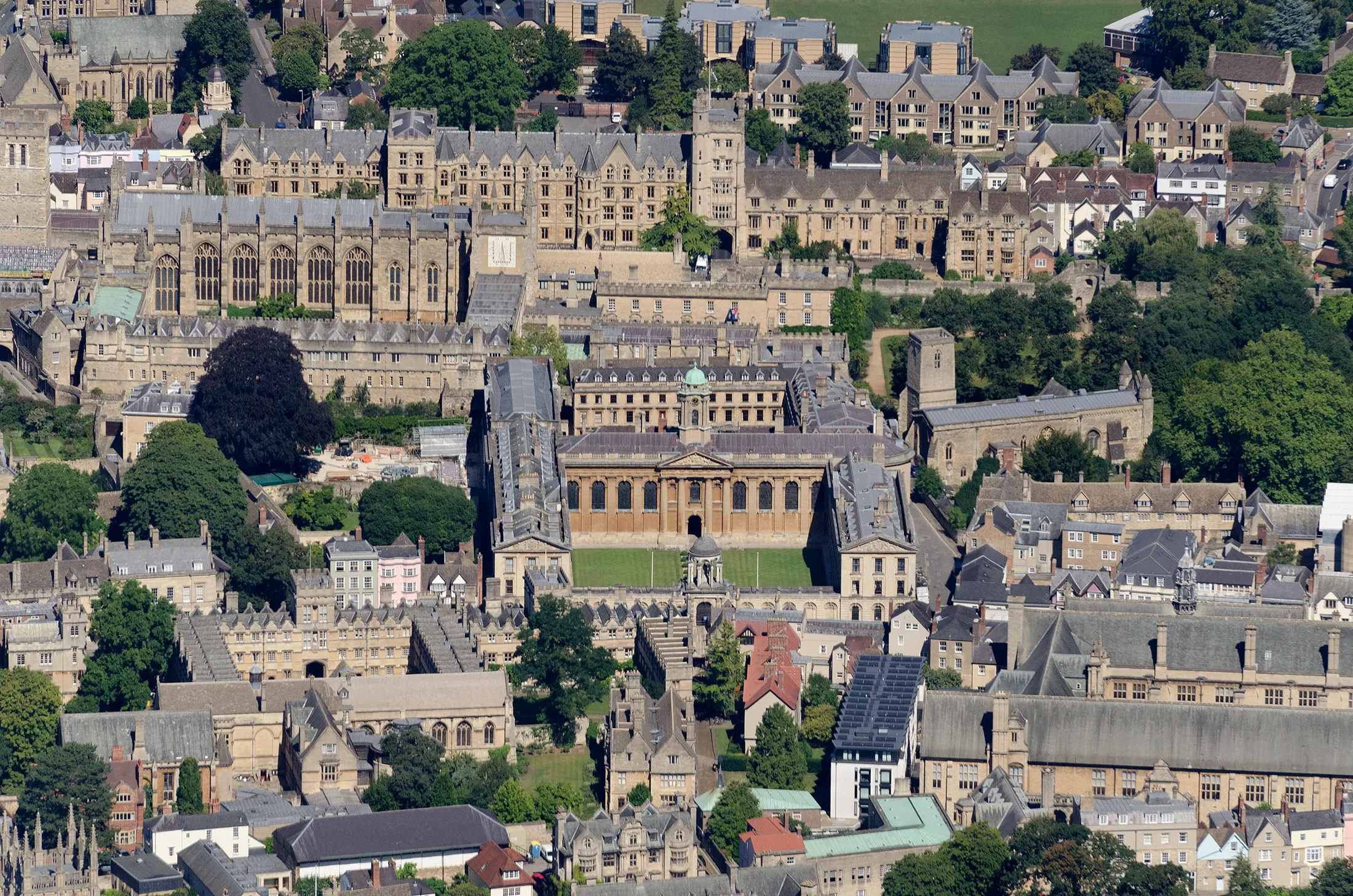 Vista aérea de The Queen's College, Oxford, mostrando su fachada barroca, sus patios, su capilla y los edificios históricos y árboles circundantes.