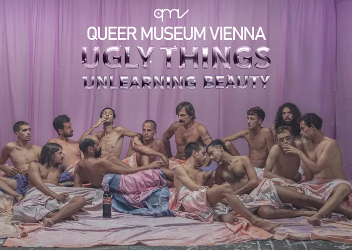 Grupa rozebranych do połowy mężczyzn zebrała się na łóżku przed fioletową zasłoną z napisem 'QUEER MUSEUM VIENNA UGLY THINGS UNLEARNING BEAUTY'.