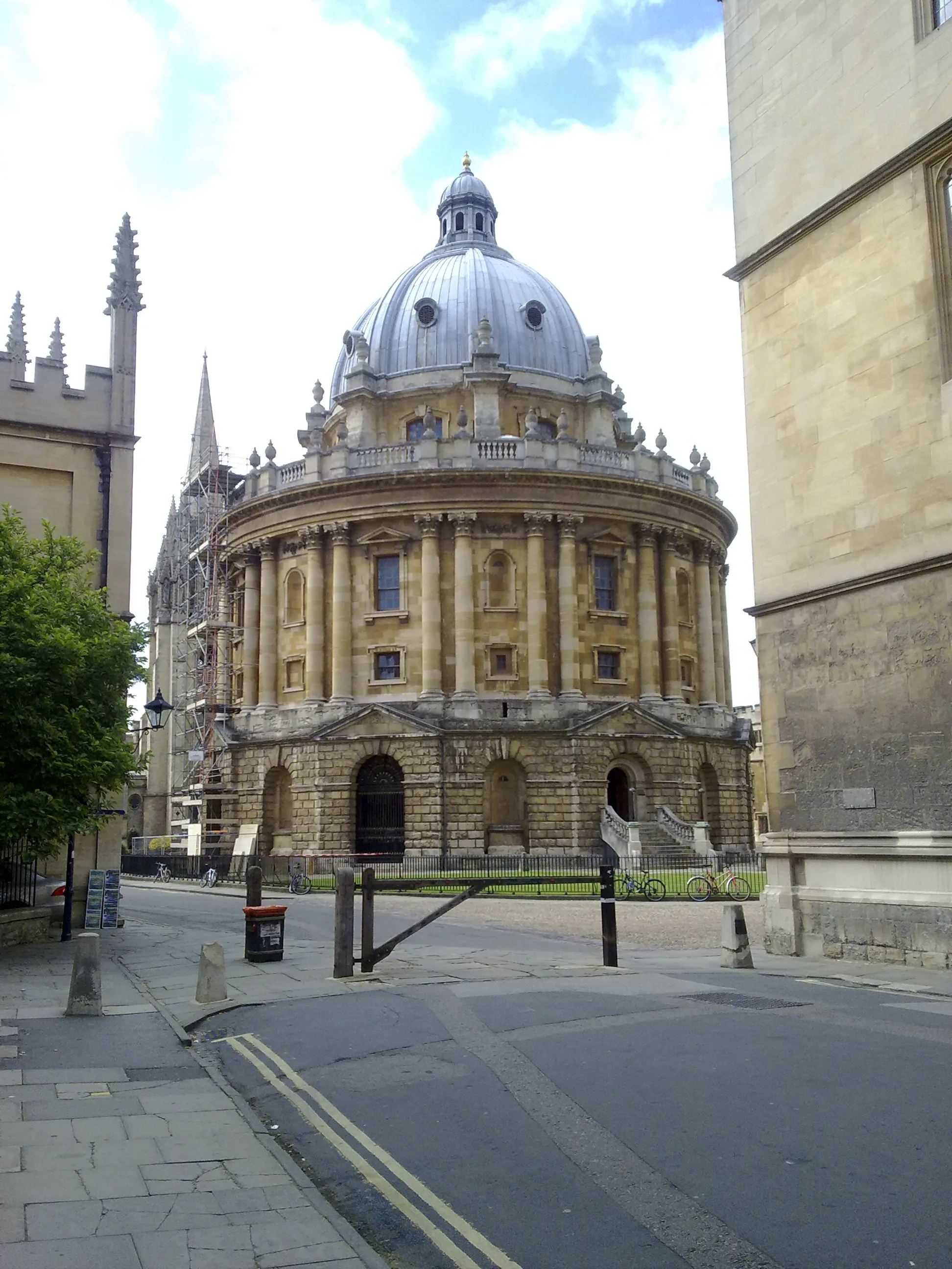 La Radcliffe Camera, un gran edificio circular de piedra con un techo abovedado, visto desde una esquina con edificios históricos adyacentes.