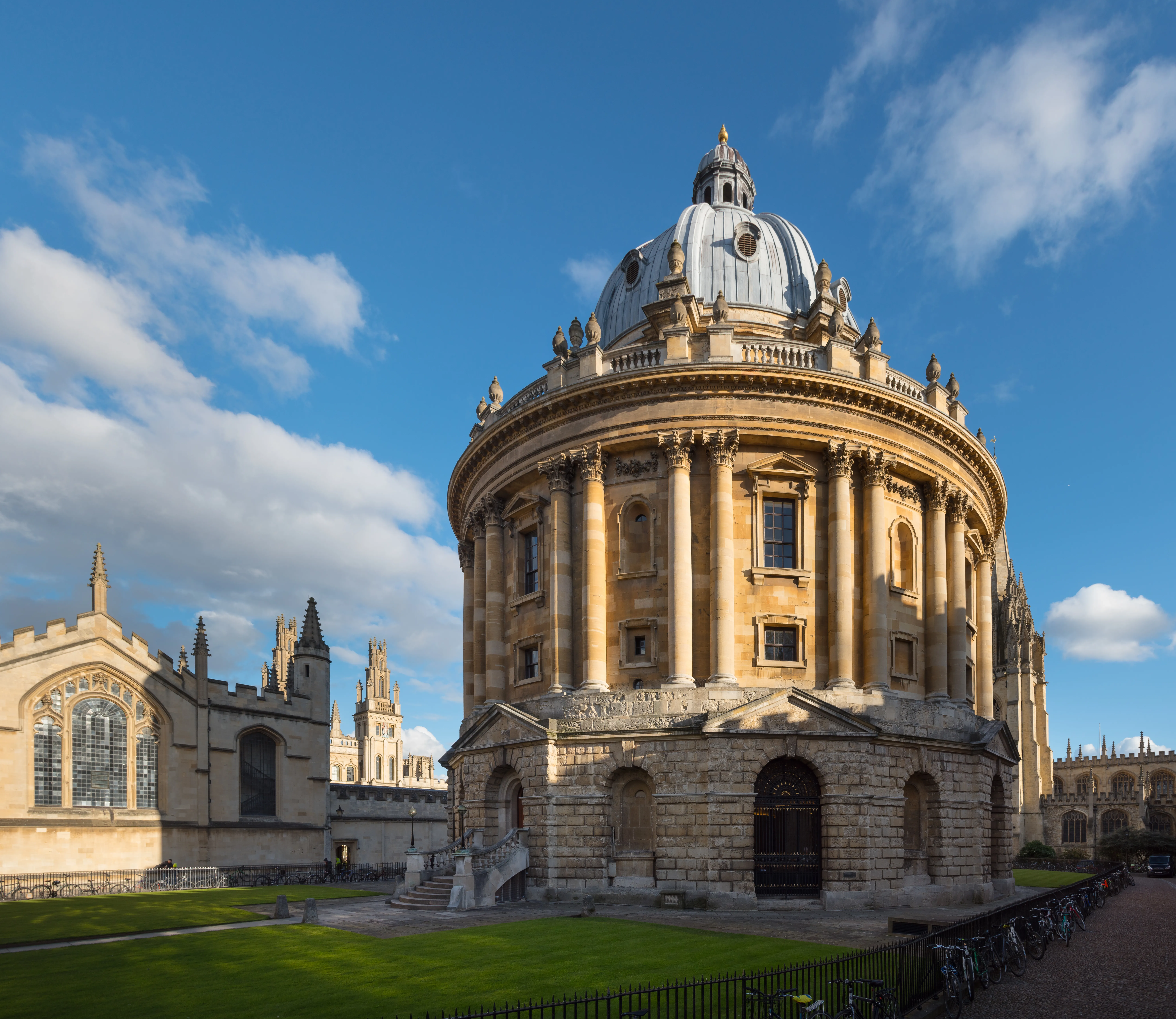 La Radcliffe Camera, un edificio bibliotecario neoclásico circular con una cúpula y columnas de piedra, bajo un cielo azul con nubes dispersas