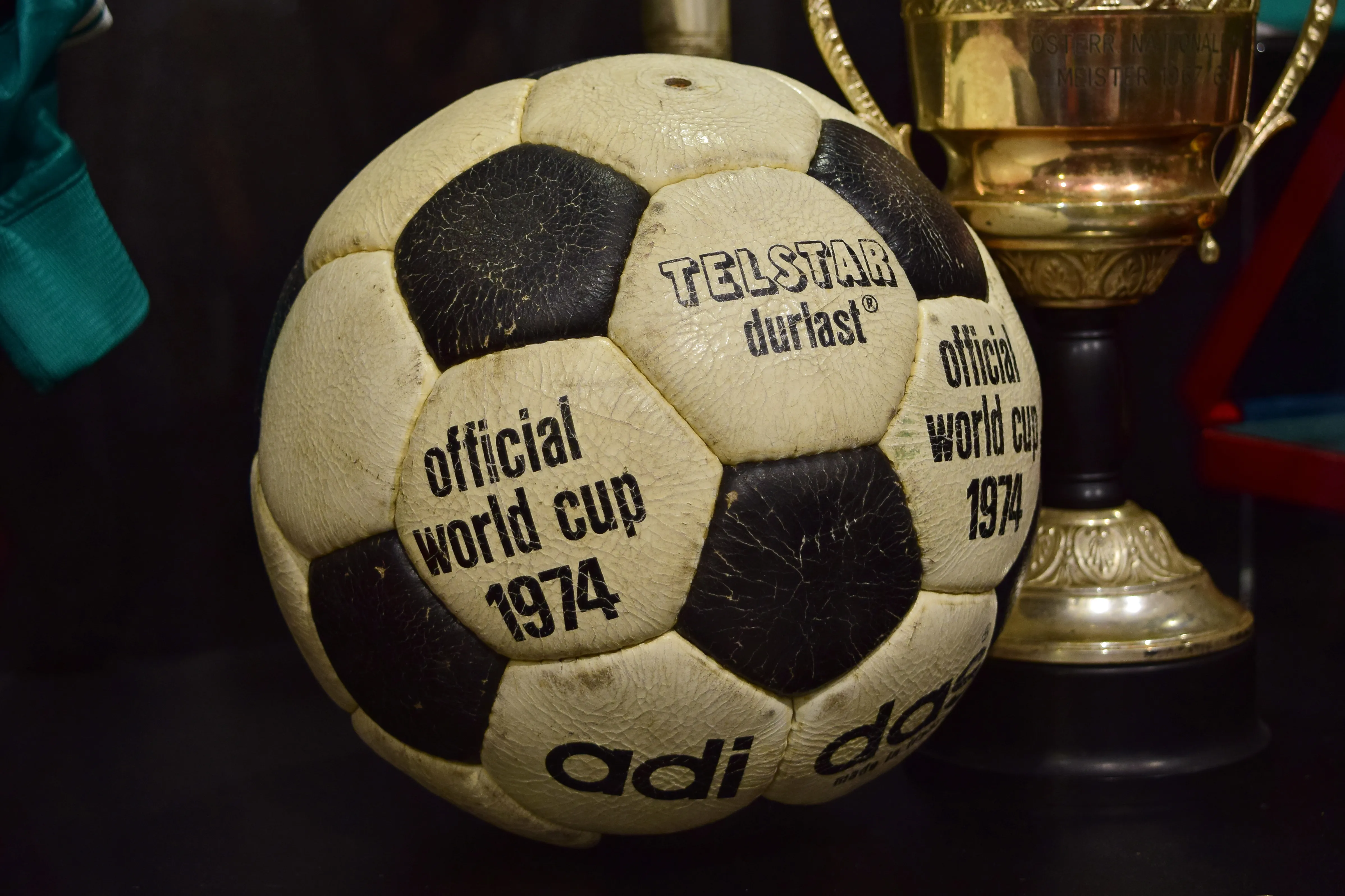 Een versleten zwart-wit voetbal met de tekst 'official world cup 1974', naast een gouden trofee