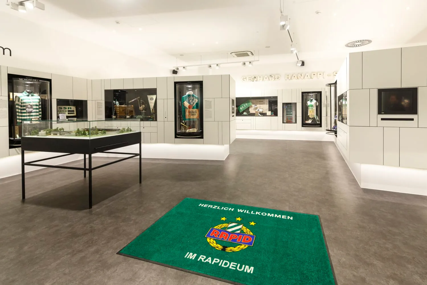 Interieur van museum het Rapideum met een groene welkomstmat, vitrines en ingelijste tentoonstellingen aan witte muren