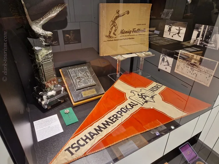 Vitrine met voetbalmemorabilia, waaronder een trofee, een vlaggetje en ingelijste foto's