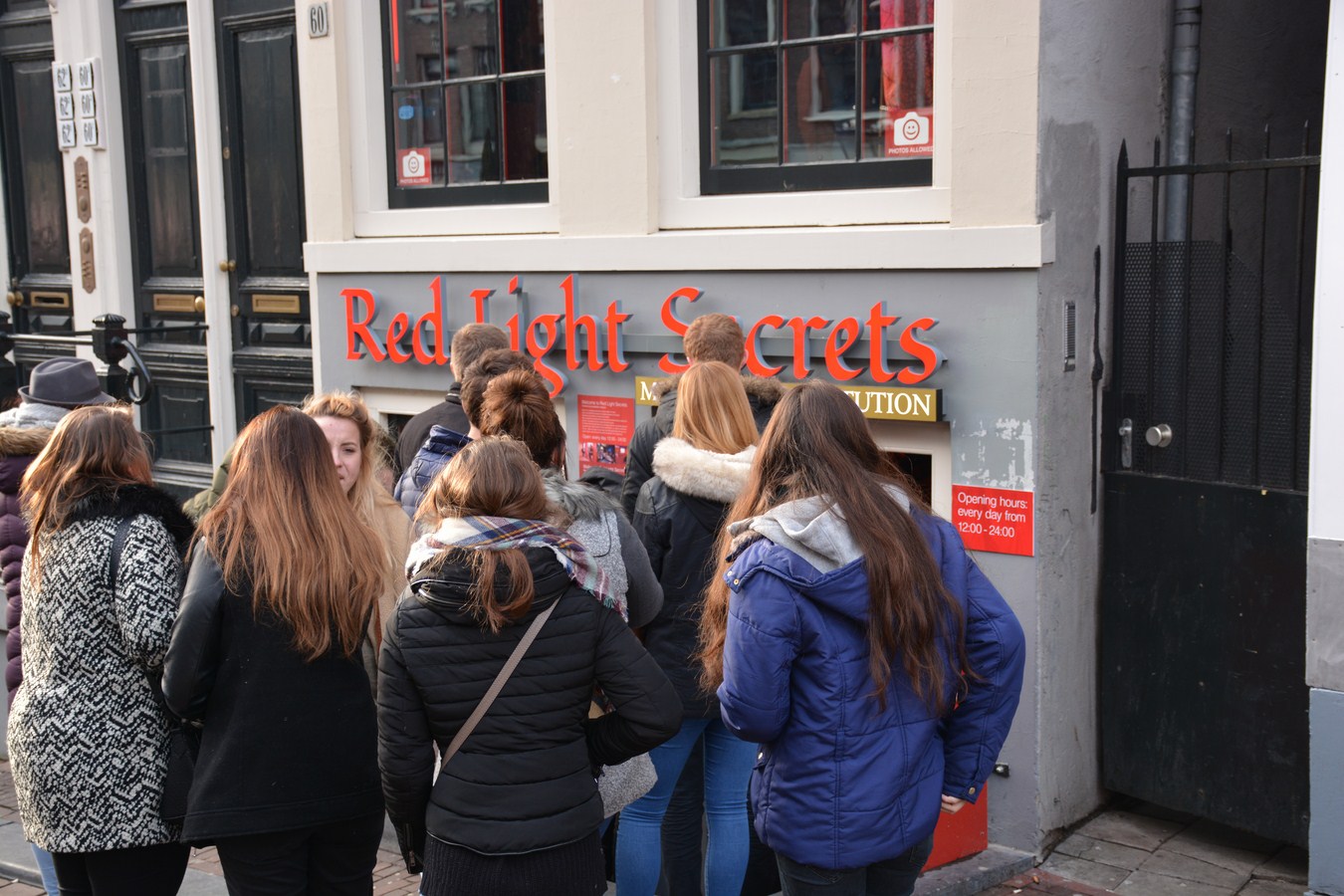 Groep bezoekers verzameld buiten de ingang van het Red Light Secrets museum met rode signage op een gevel in Amsterdam