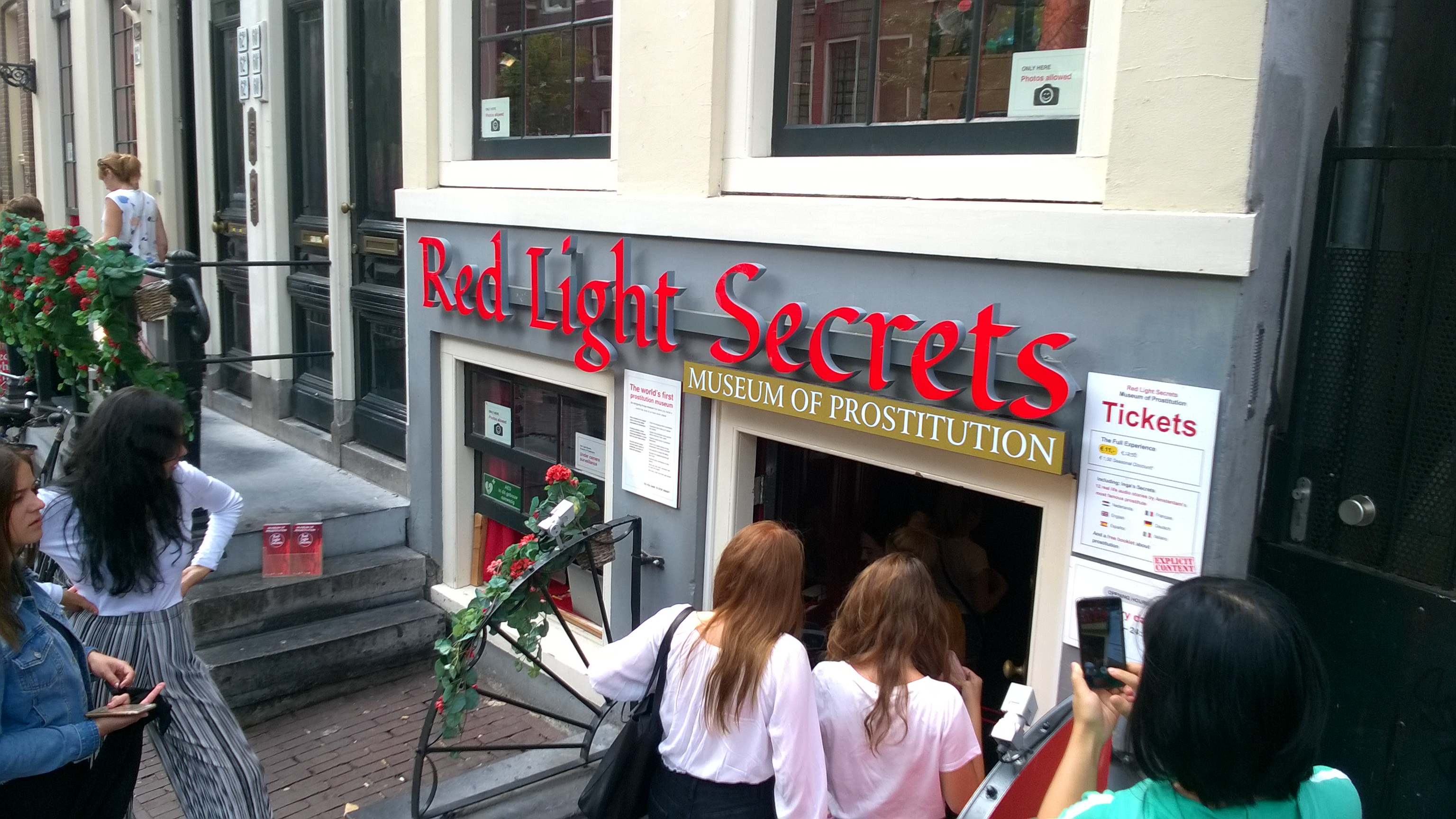 Buitenkant van Red Light Secrets Museum of Prostitution in Amsterdam met rode bewegwijzering en mensen die het gebouw betreden