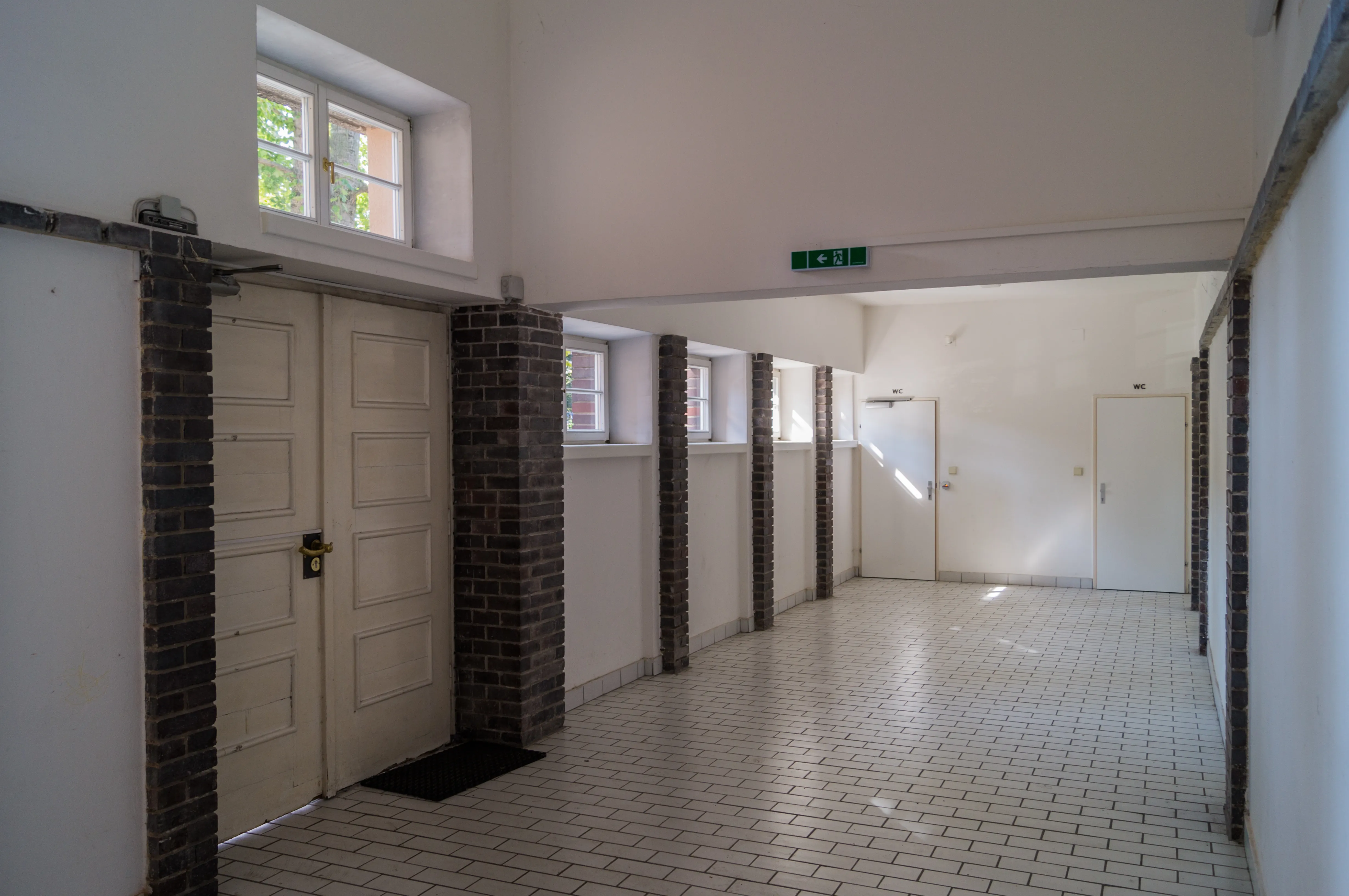 Pasillo interior con suelos de baldosas blancas, puertas blancas y pilares de ladrillo