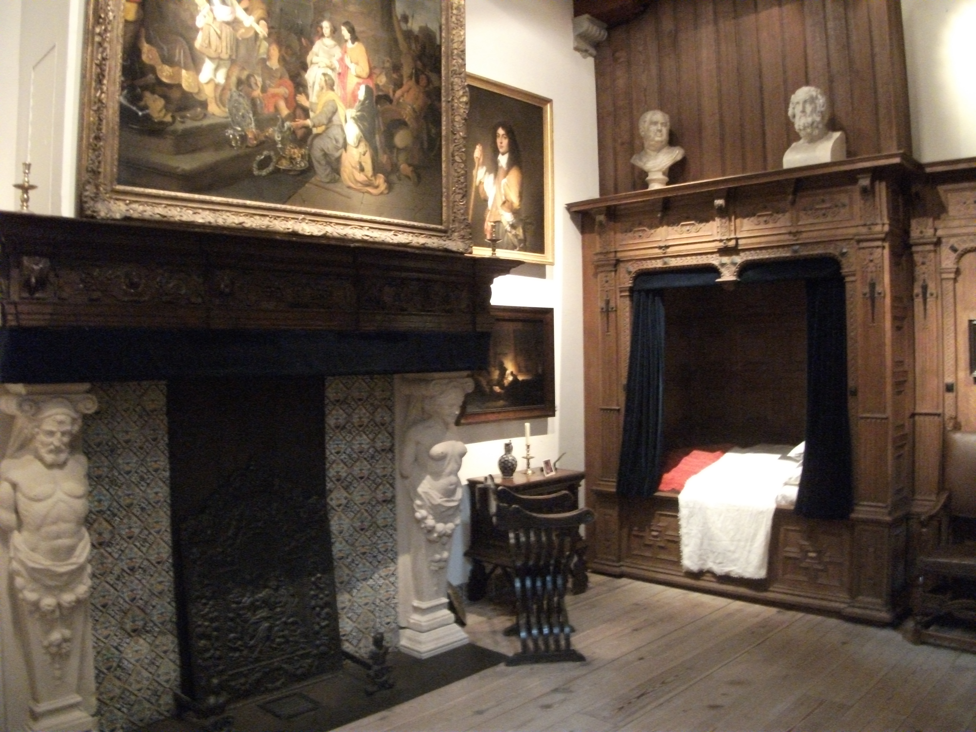 Historyczny pokój z drewnianą boazerią, ozdobnym kominkiem, obrazami na ścianach i zabytkowymi meblami w Muzeum Dom Rembrandta