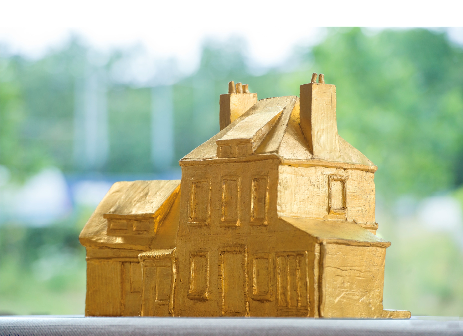 Modelo en miniatura dorado de una casa de canal holandesa con frontones escalonados y múltiples chimeneas sobre un fondo verde desenfocado