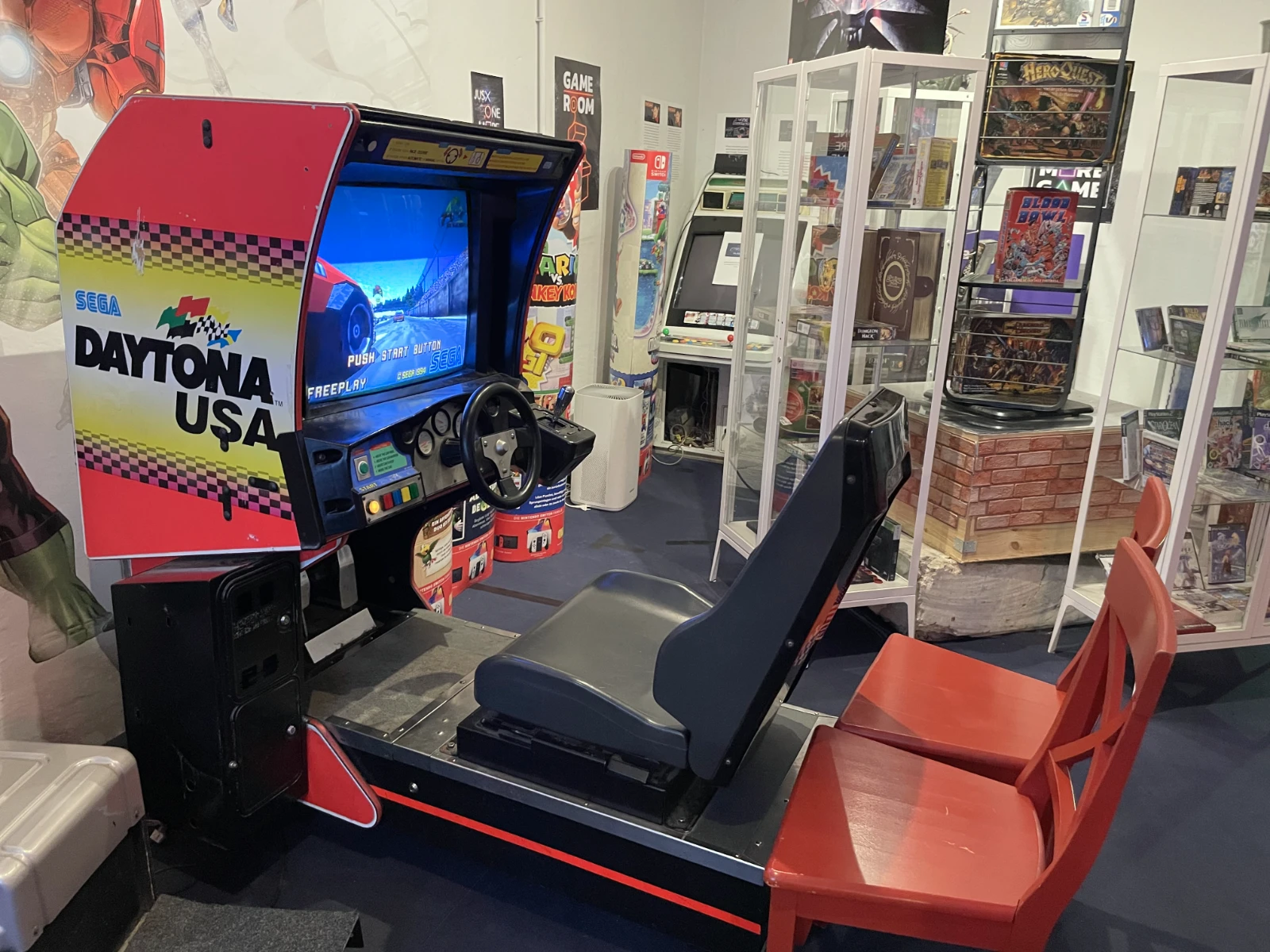 Una máquina arcade Daytona USA roja con volante y asiento de conductor en un entorno de museo