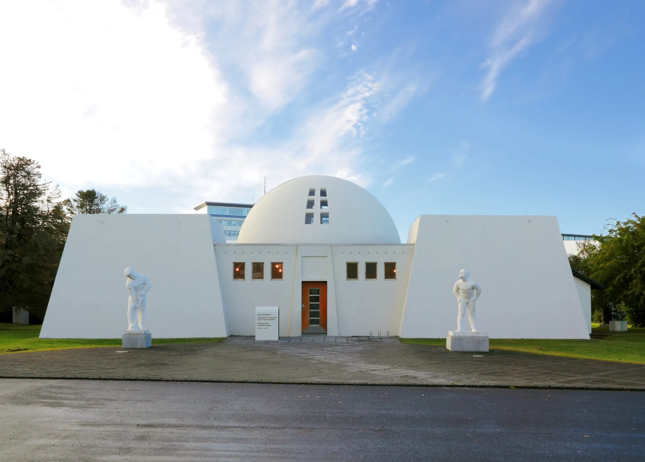 Edificio de cúpula blanca de Ásmundarsafn con dos esculturas blancas flanqueando la entrada bajo un cielo azul