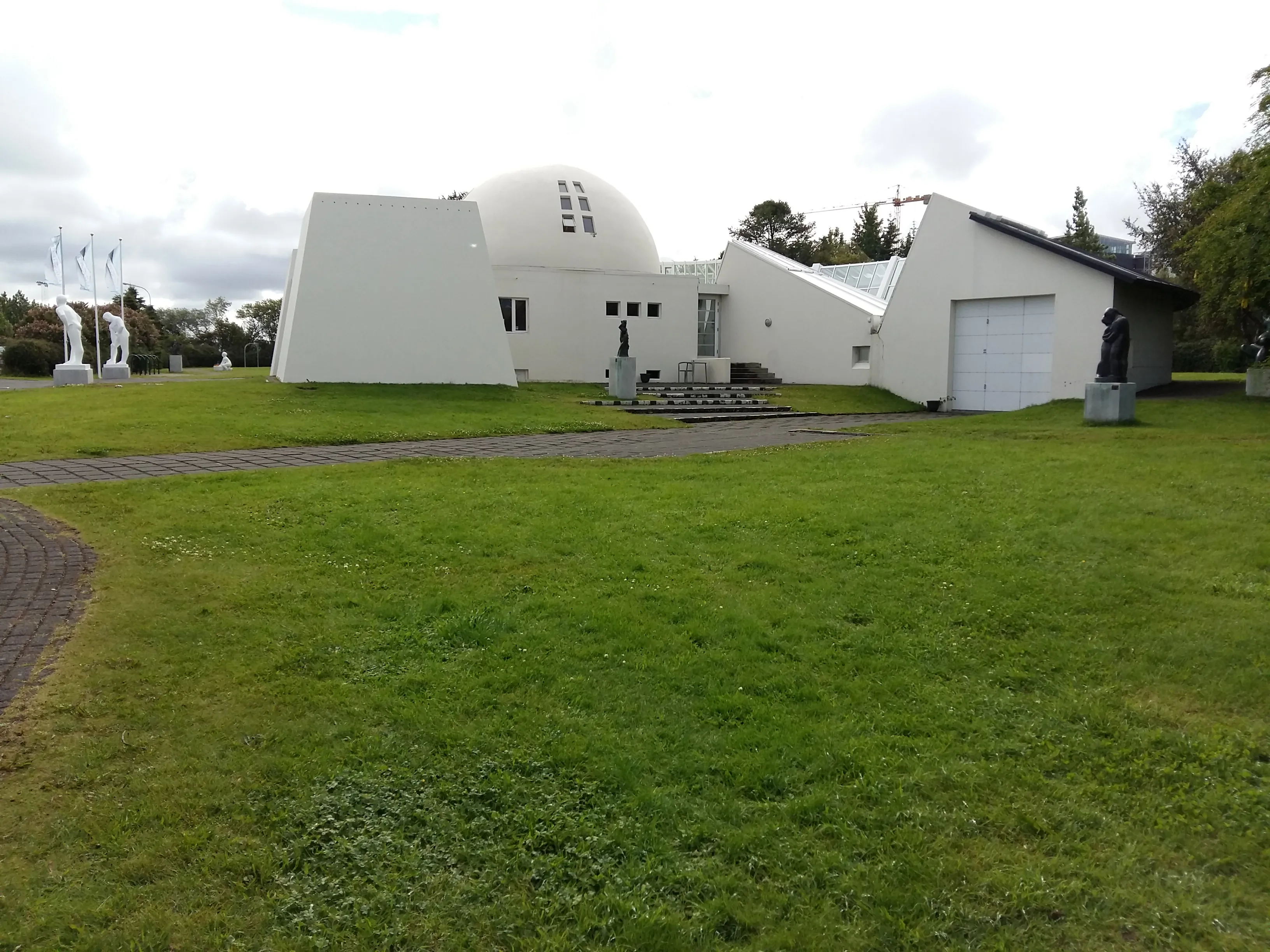 Edificio blanco con una cúpula y alas angulares rodeado de césped verde y esculturas al aire libre en el museo Ásmundarsafn